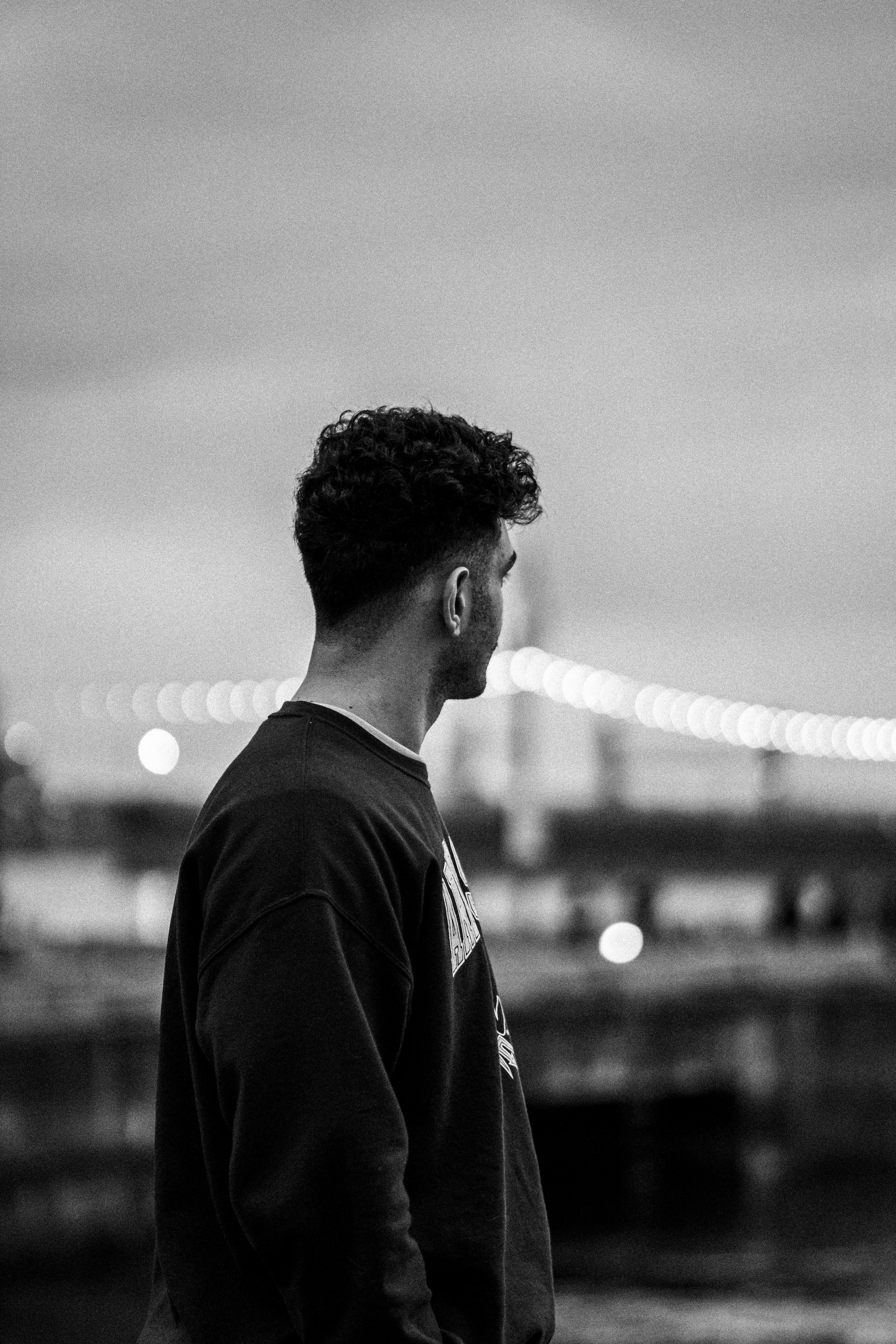 A person in a dark sweatshirt looking toward a blurred suspension bridge