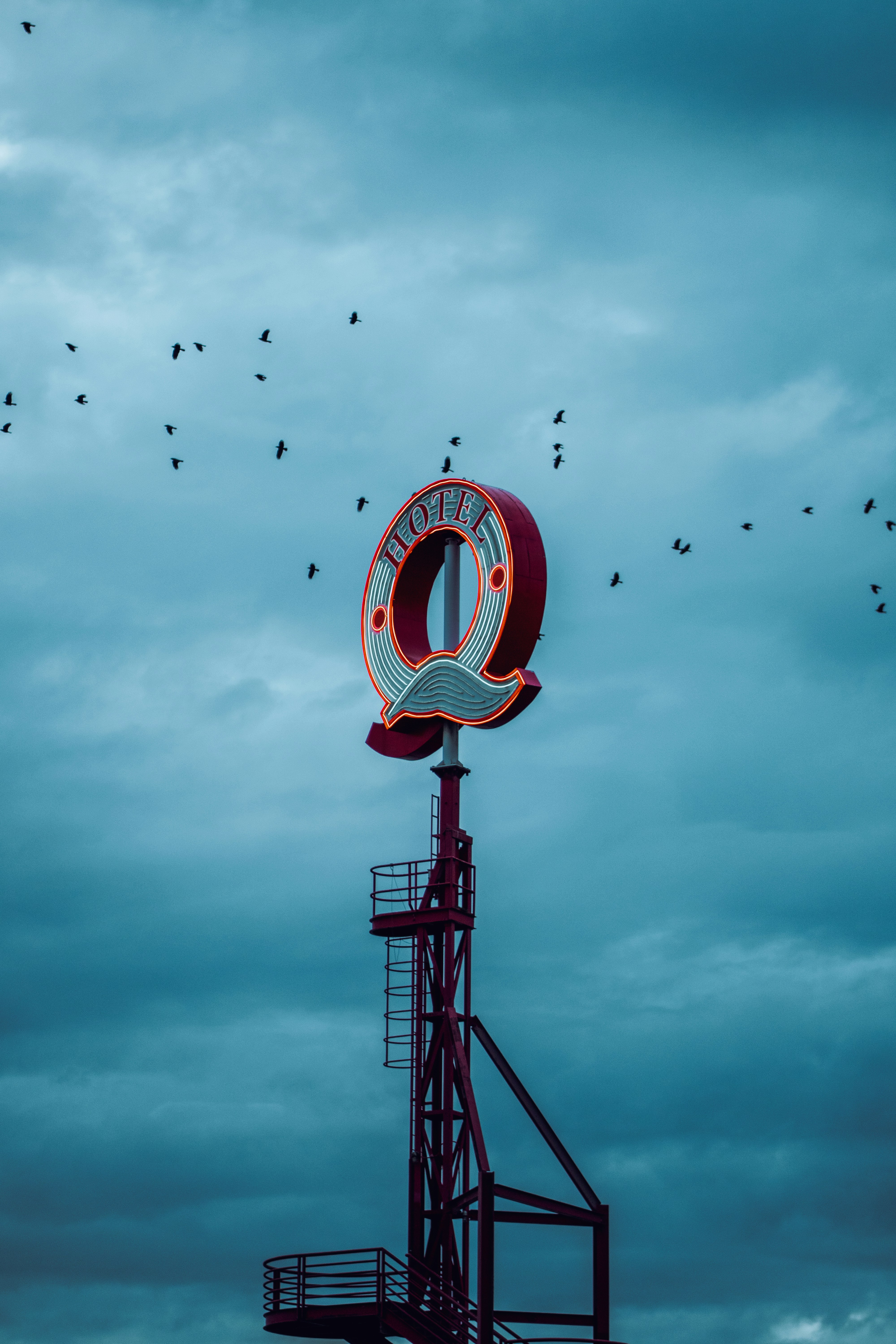 A large red neon hotel sign shaped like a Q against a cloudy sky