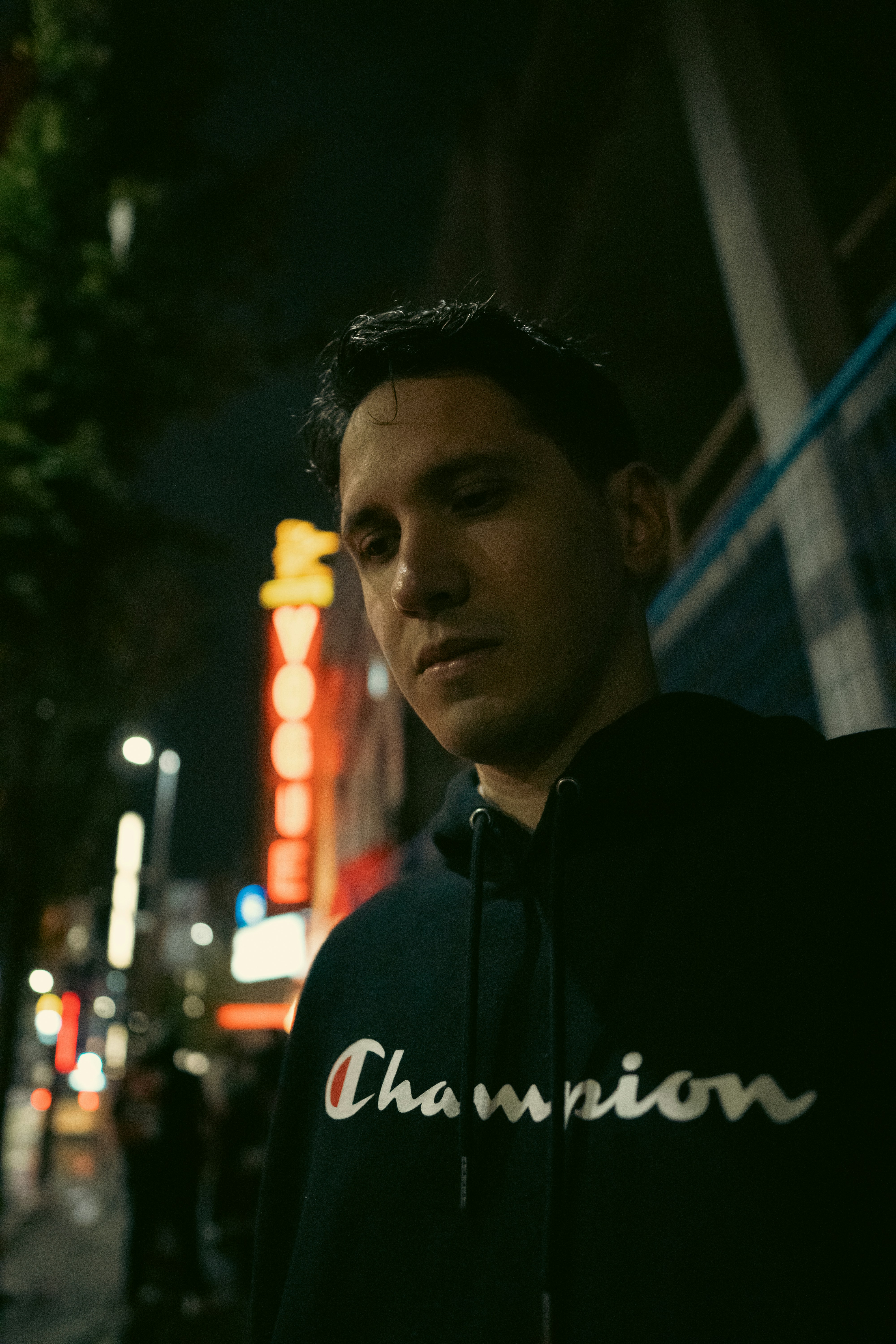 A man in a black hoodie standing on a city street at night