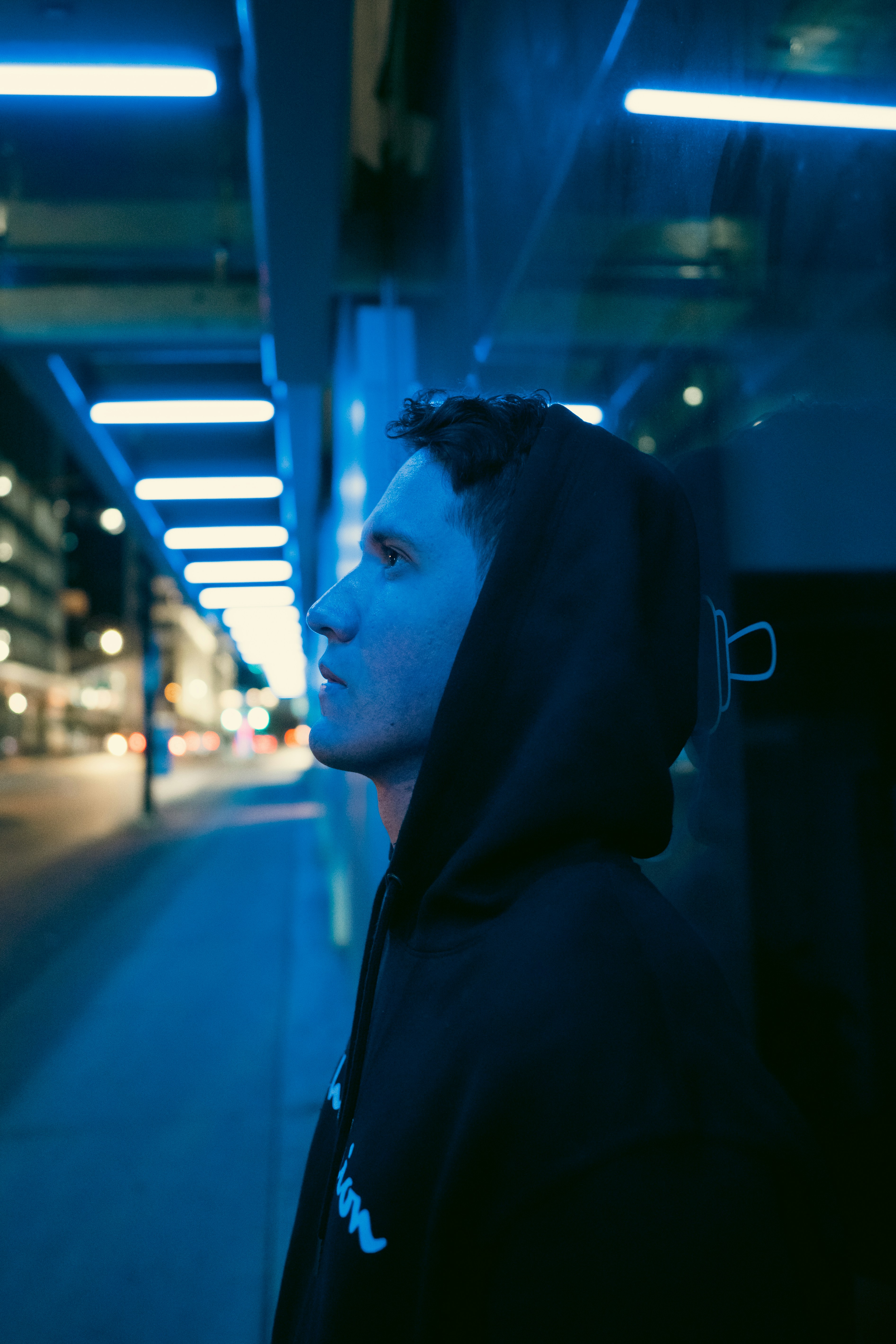 A man in a black hoodie on a city street at night under blue lights