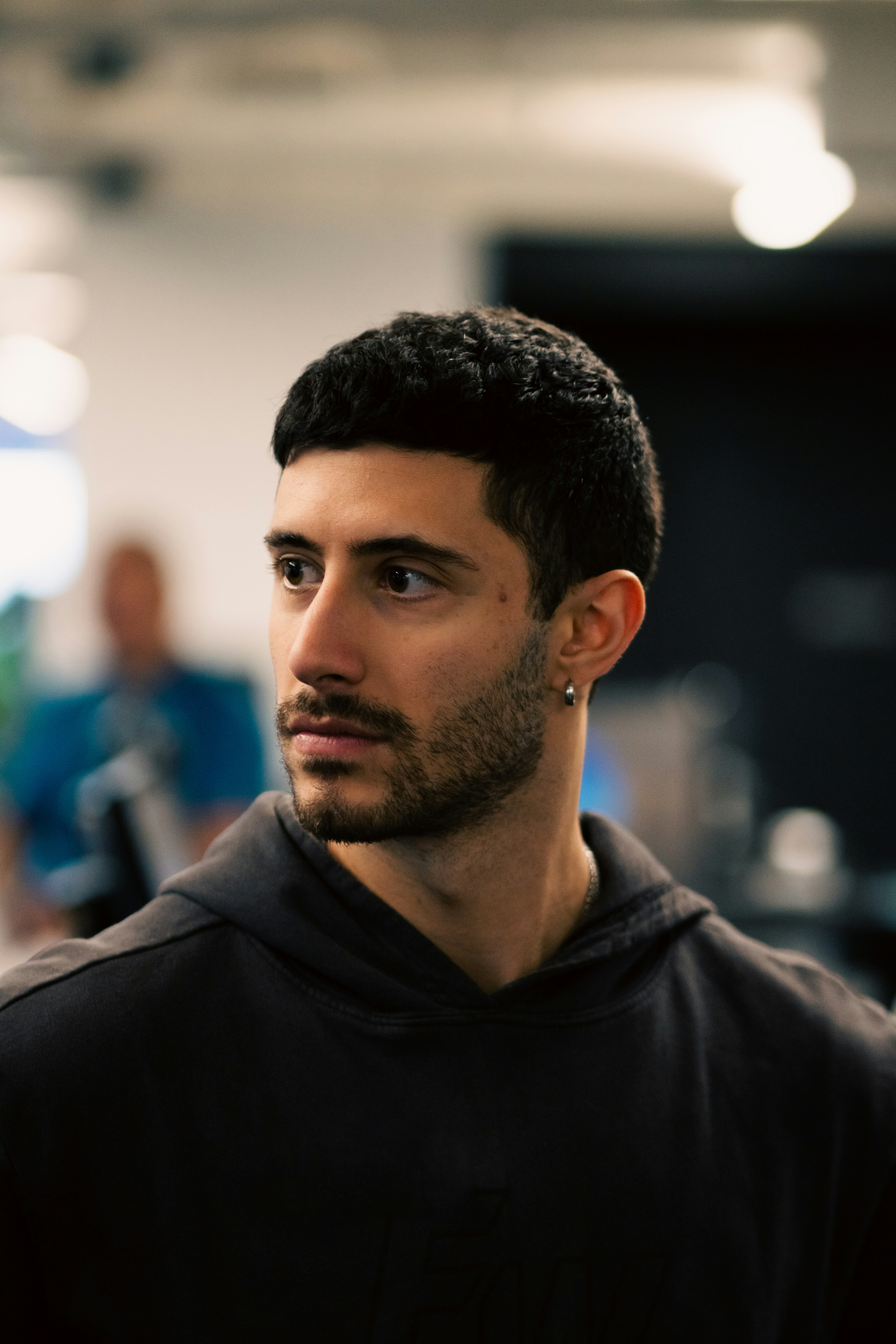 A man with short dark hair and a beard wearing a dark hoodie