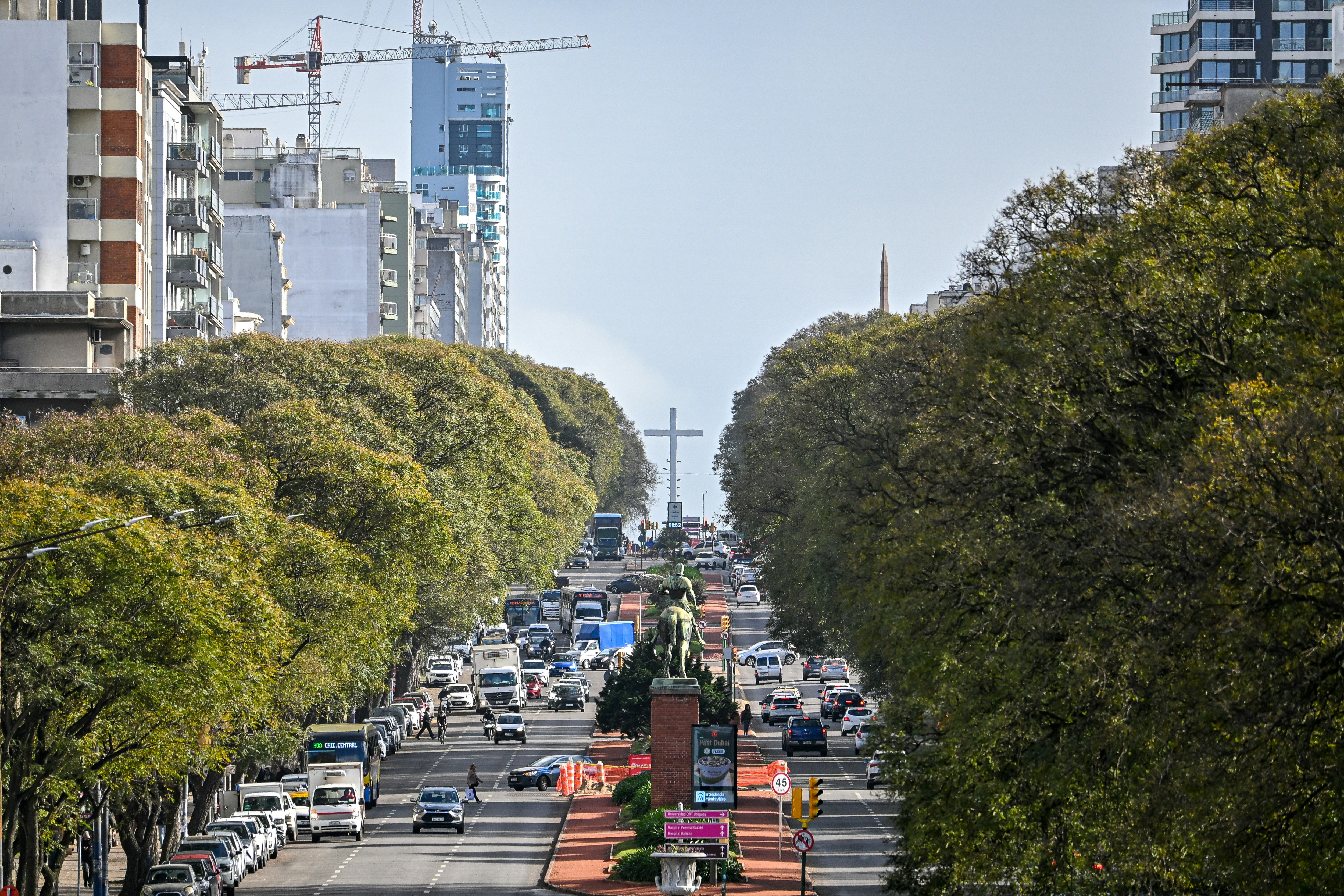 Traffic on a tree-lined avenue in Buenos Aires with a large cross in distance