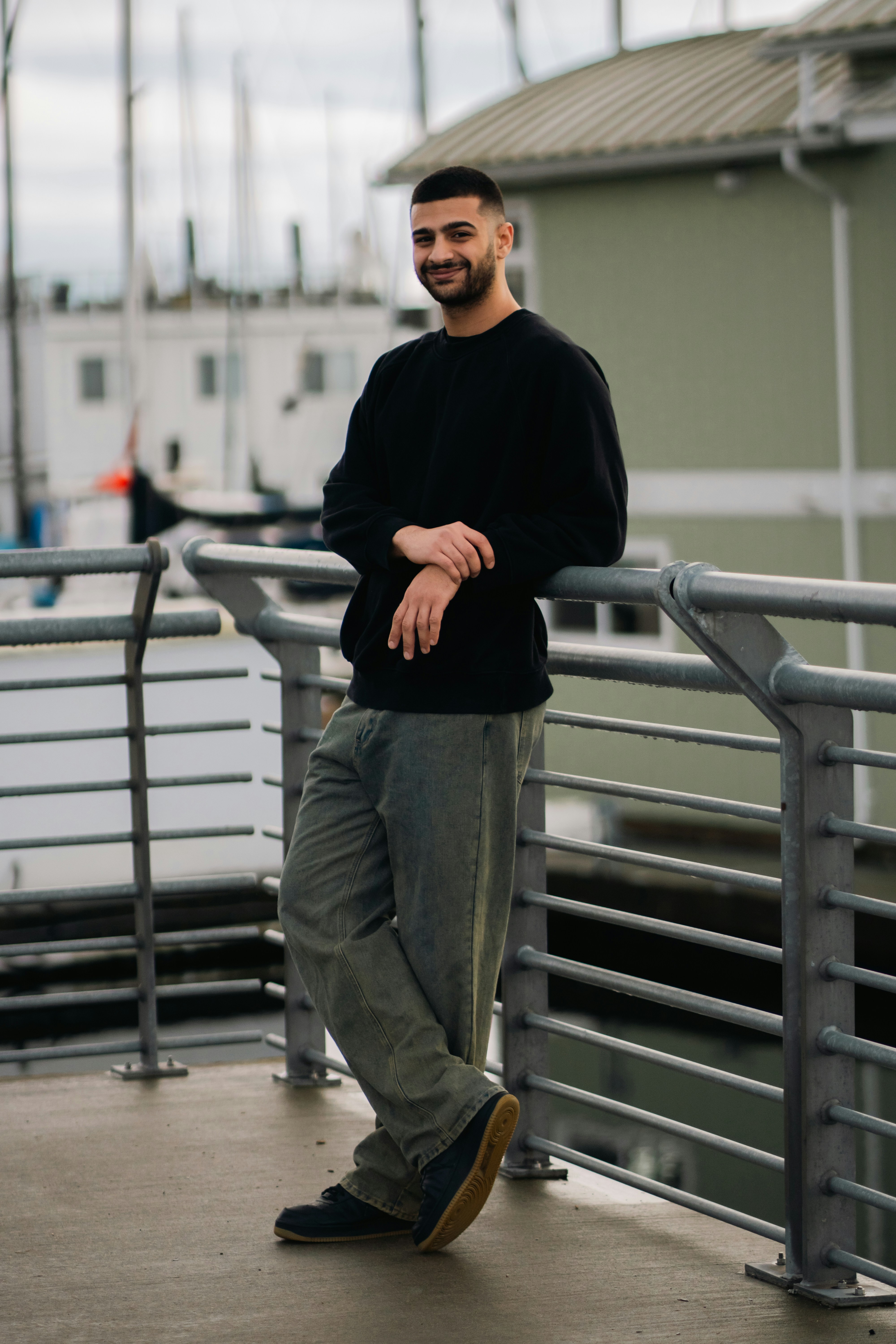 A man in a black sweatshirt and jeans leaning against a metal railing