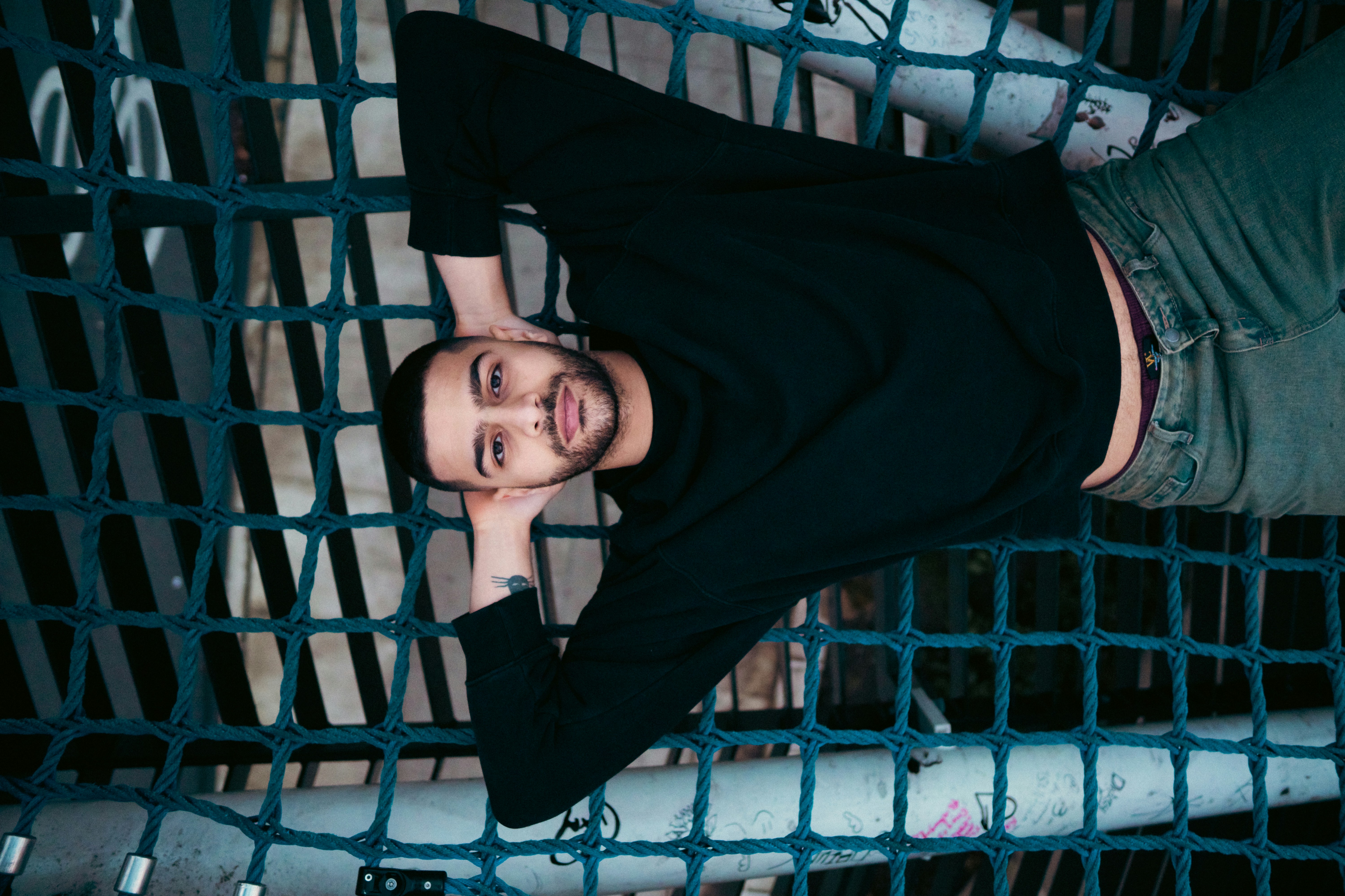 A man in a black sweatshirt lying on a blue rope climbing net