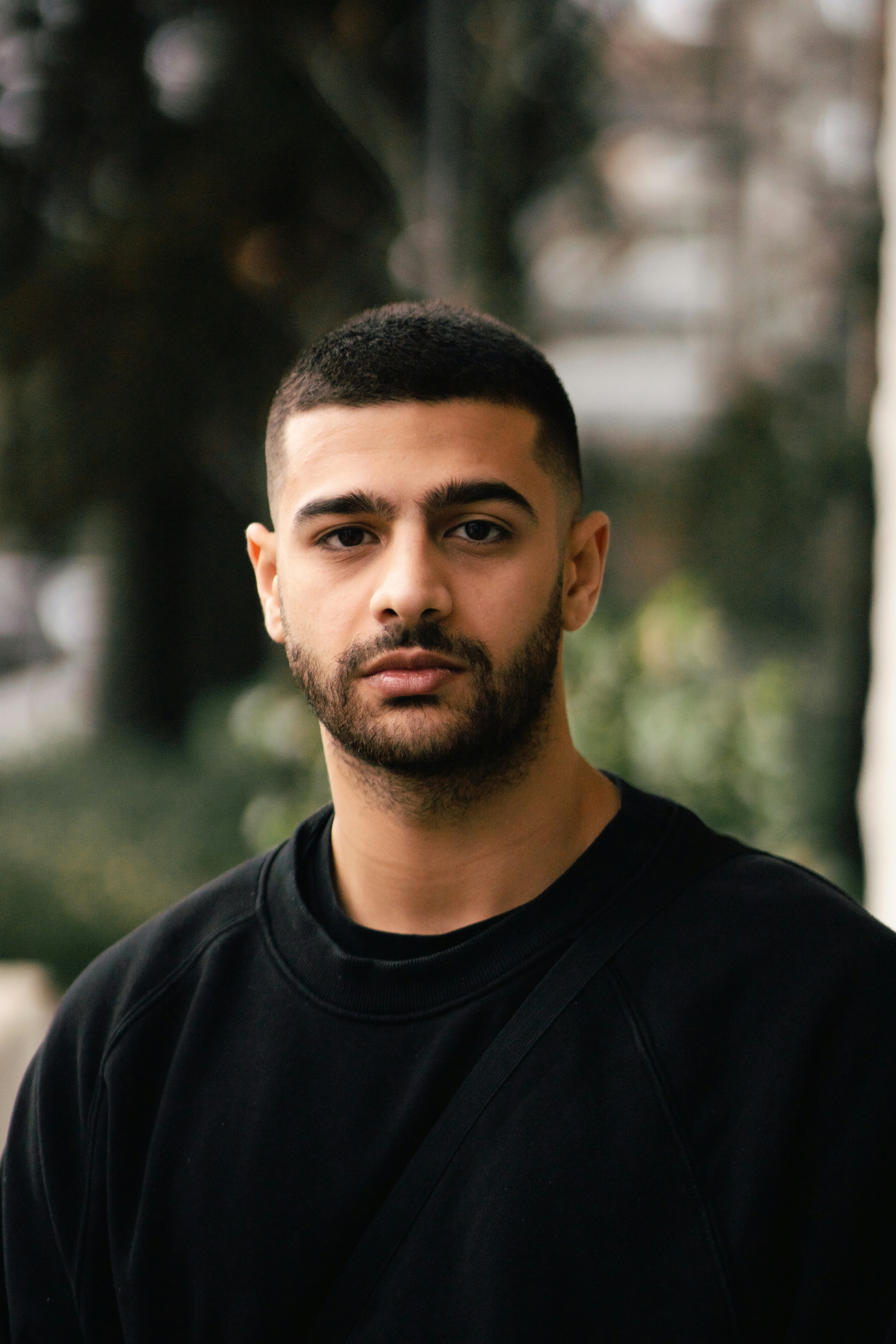 A man with a short haircut and beard in a black sweatshirt outdoors