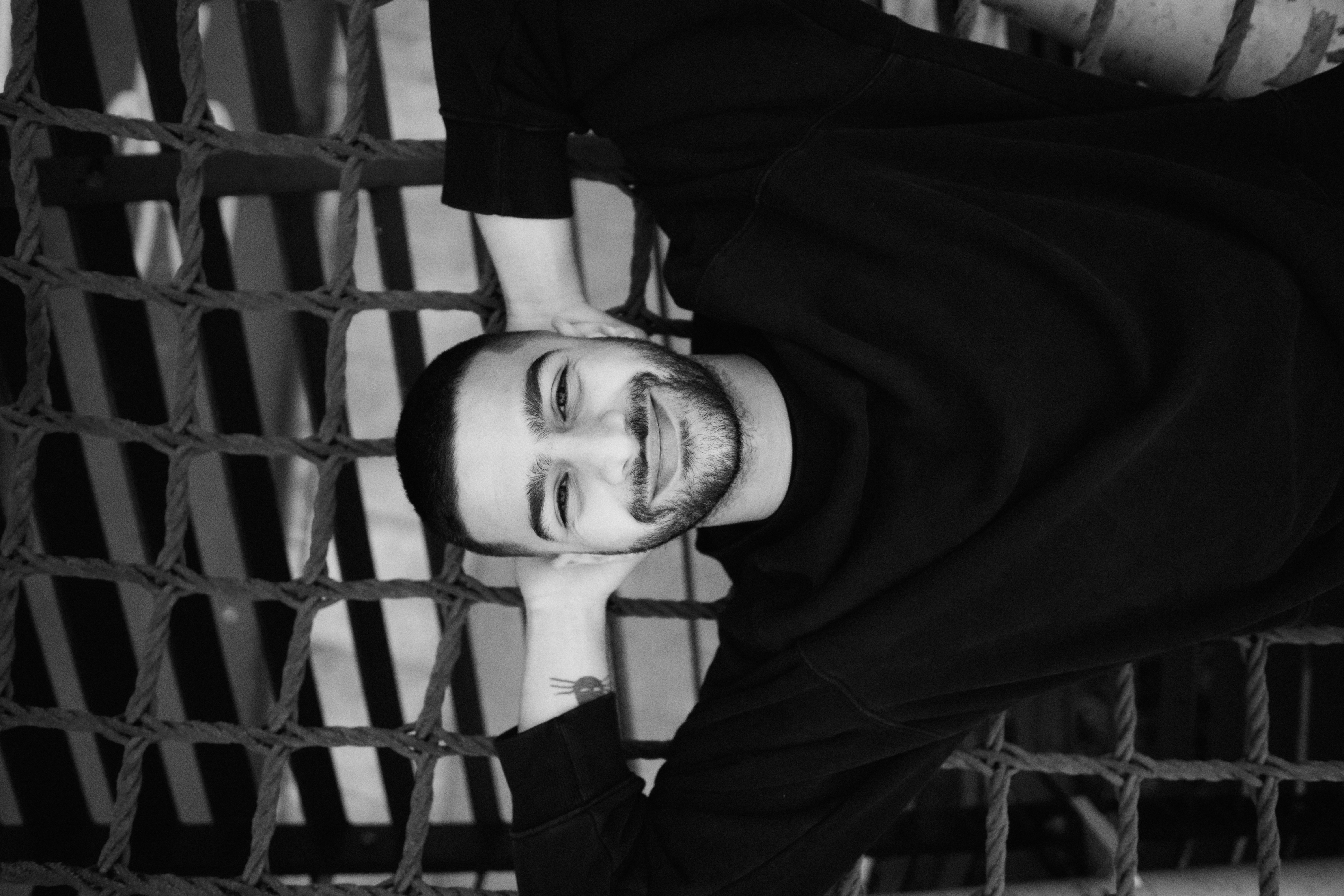 A man with a beard in a black sweatshirt lying on a rope net