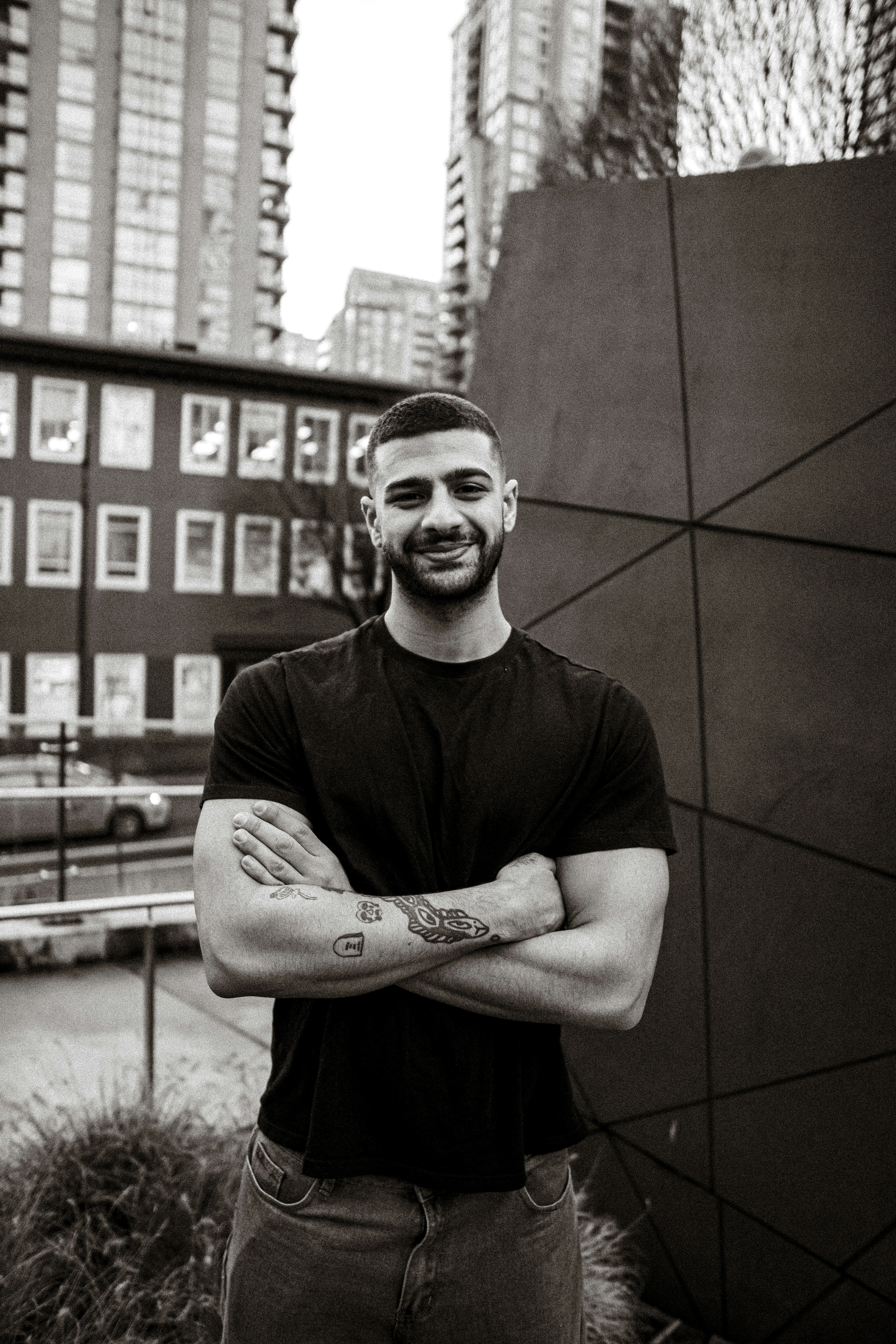 A man with short hair and tattoos on his arms standing with crossed arms