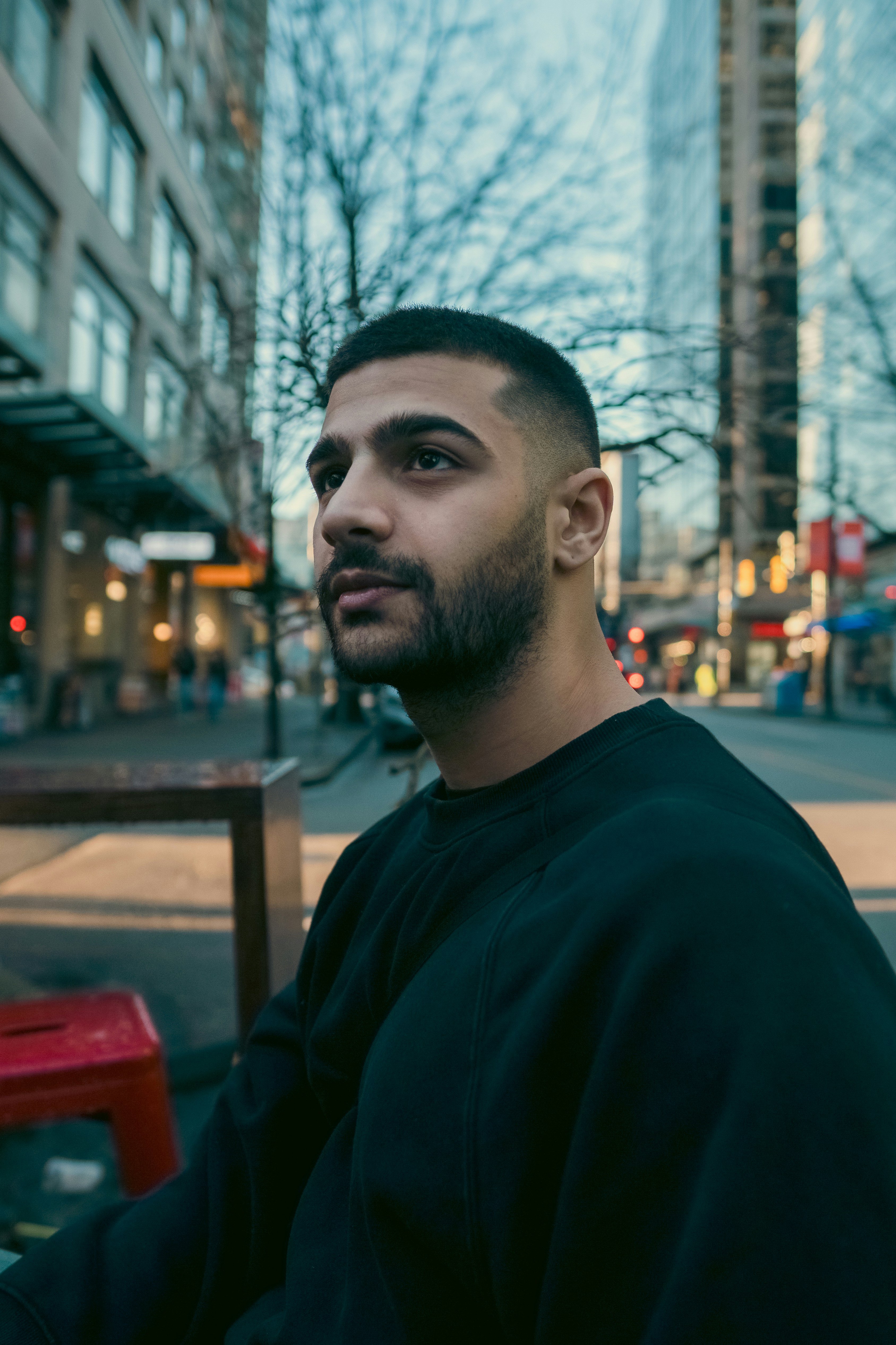 A man with a short beard in a black sweatshirt on a city street