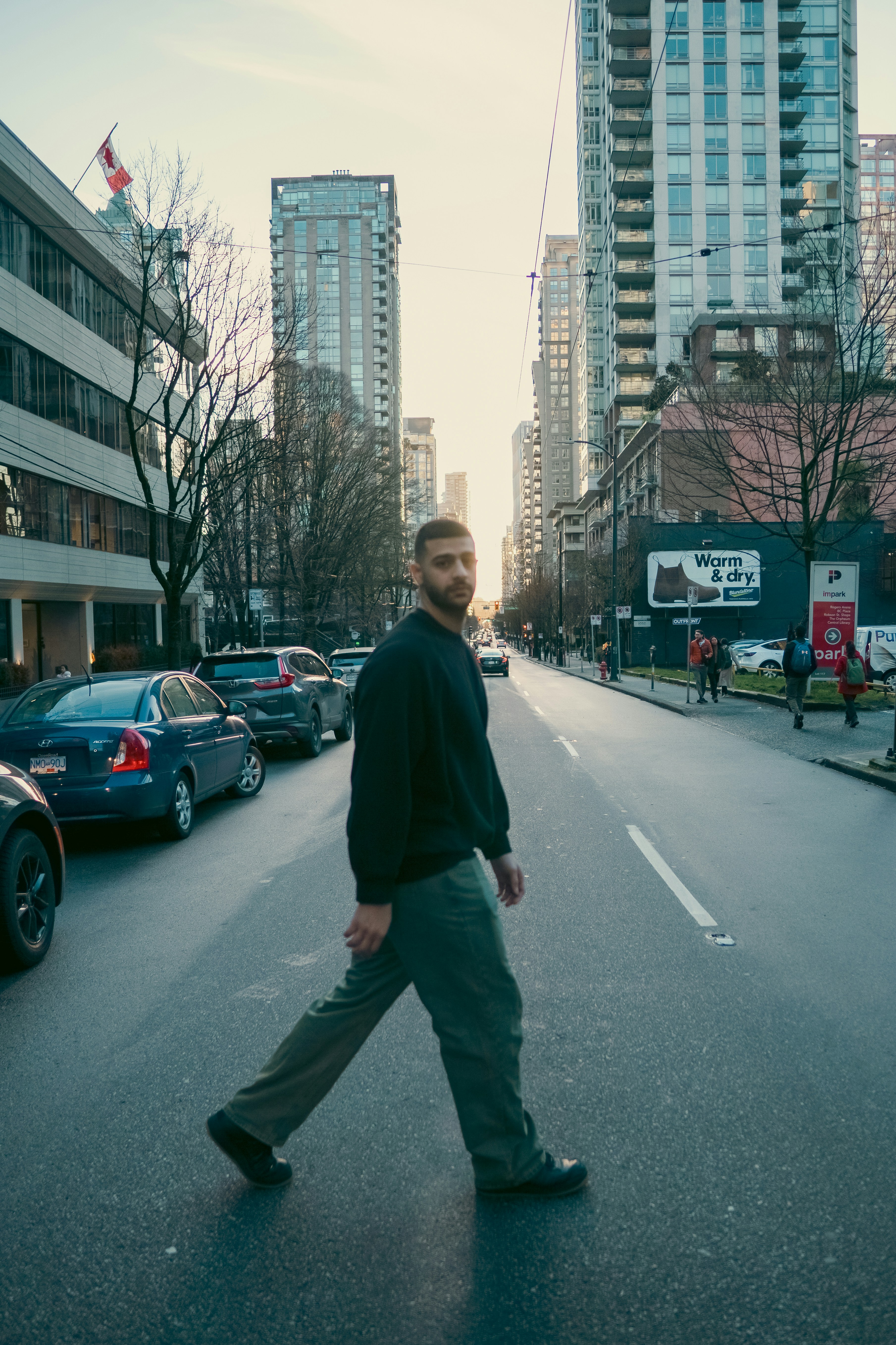 A man in a dark sweater crossing a city street between tall buildings