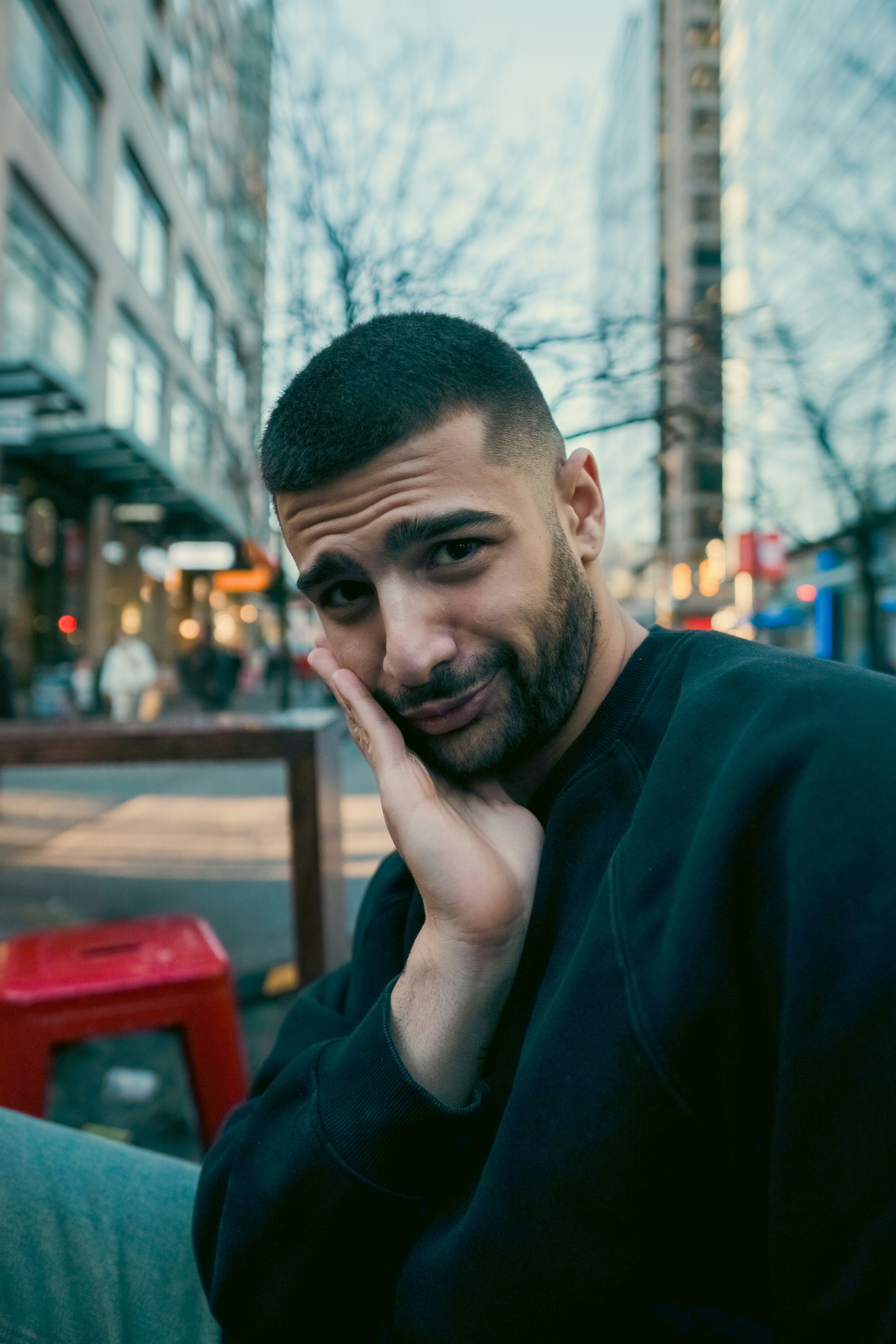 A man with a short beard and dark sweatshirt resting his face on his hand