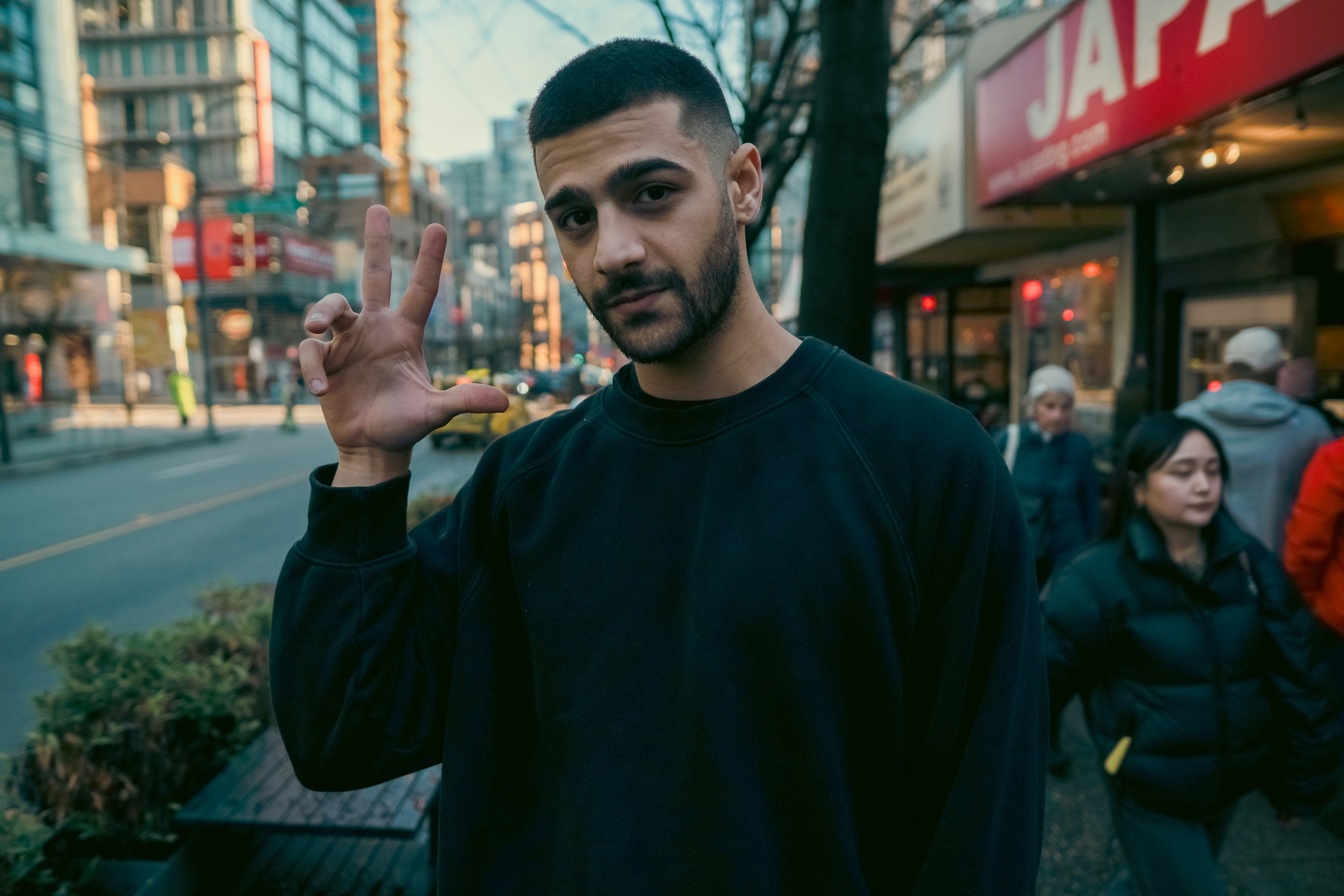 A man in a black sweatshirt making a hand gesture on a city street