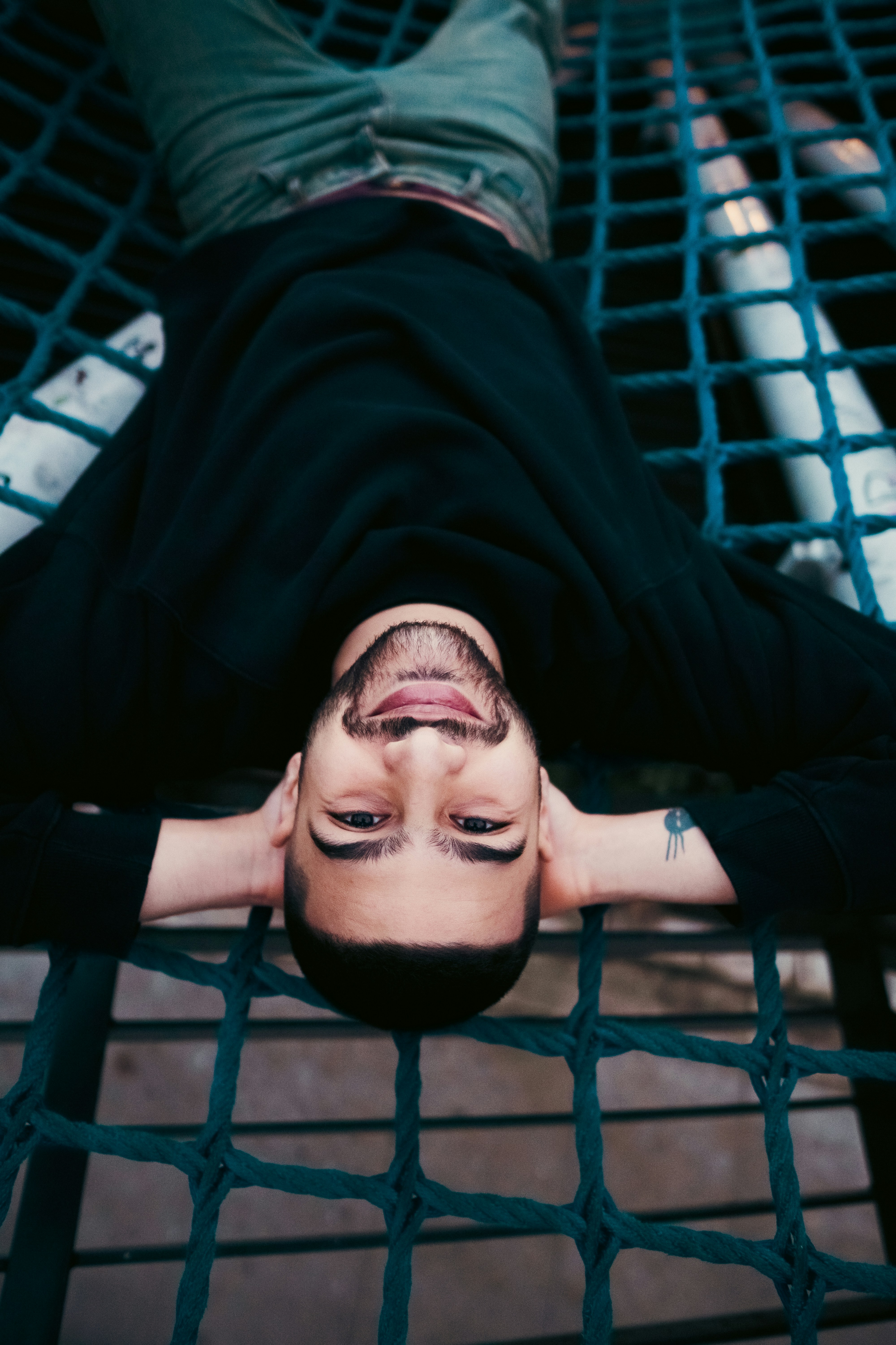 A man with a beard lying on a blue rope hammock