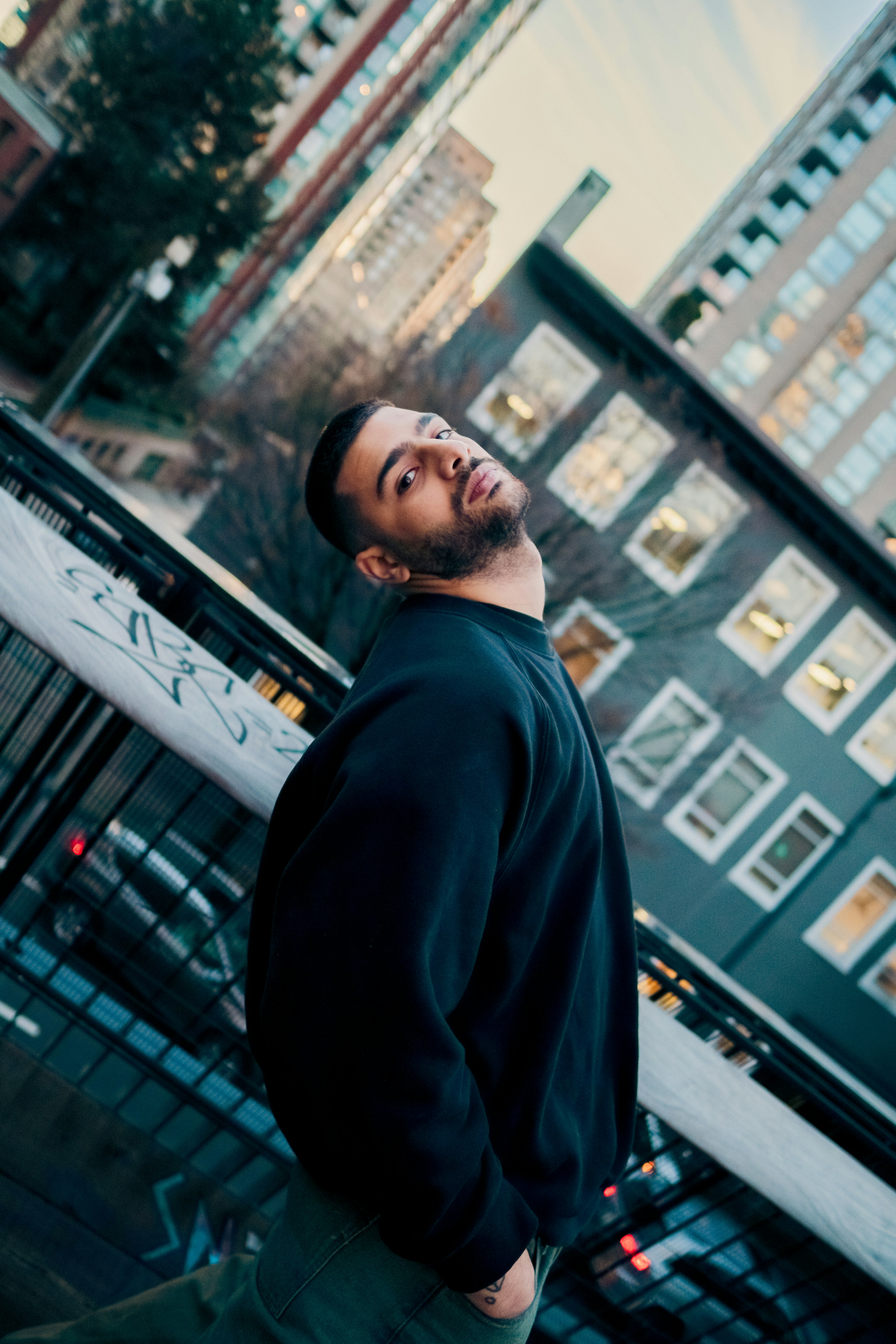 A man in a black sweatshirt leaning against a railing in a city