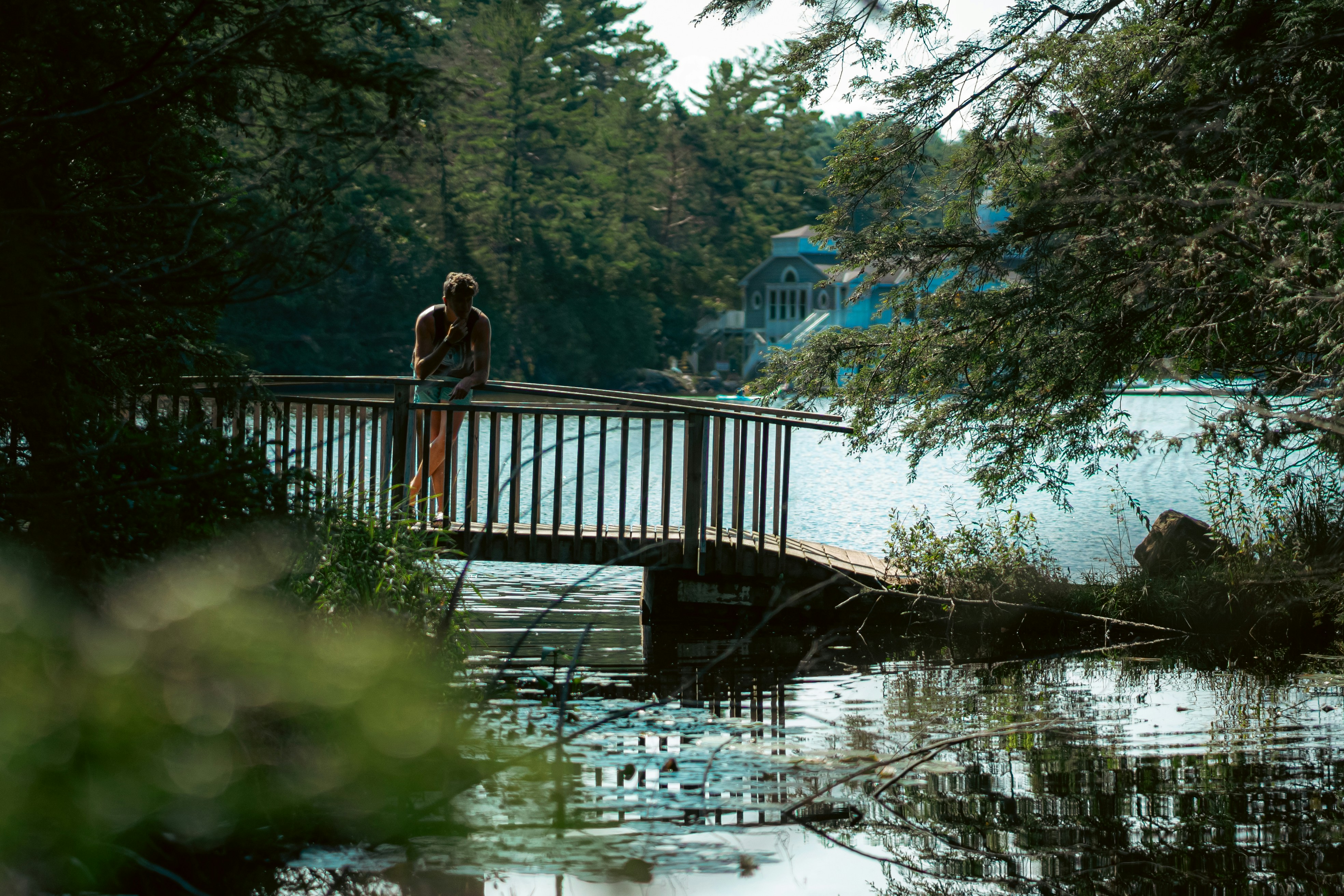 A person leaning on a wooden footbridge over a calm lake in a forest