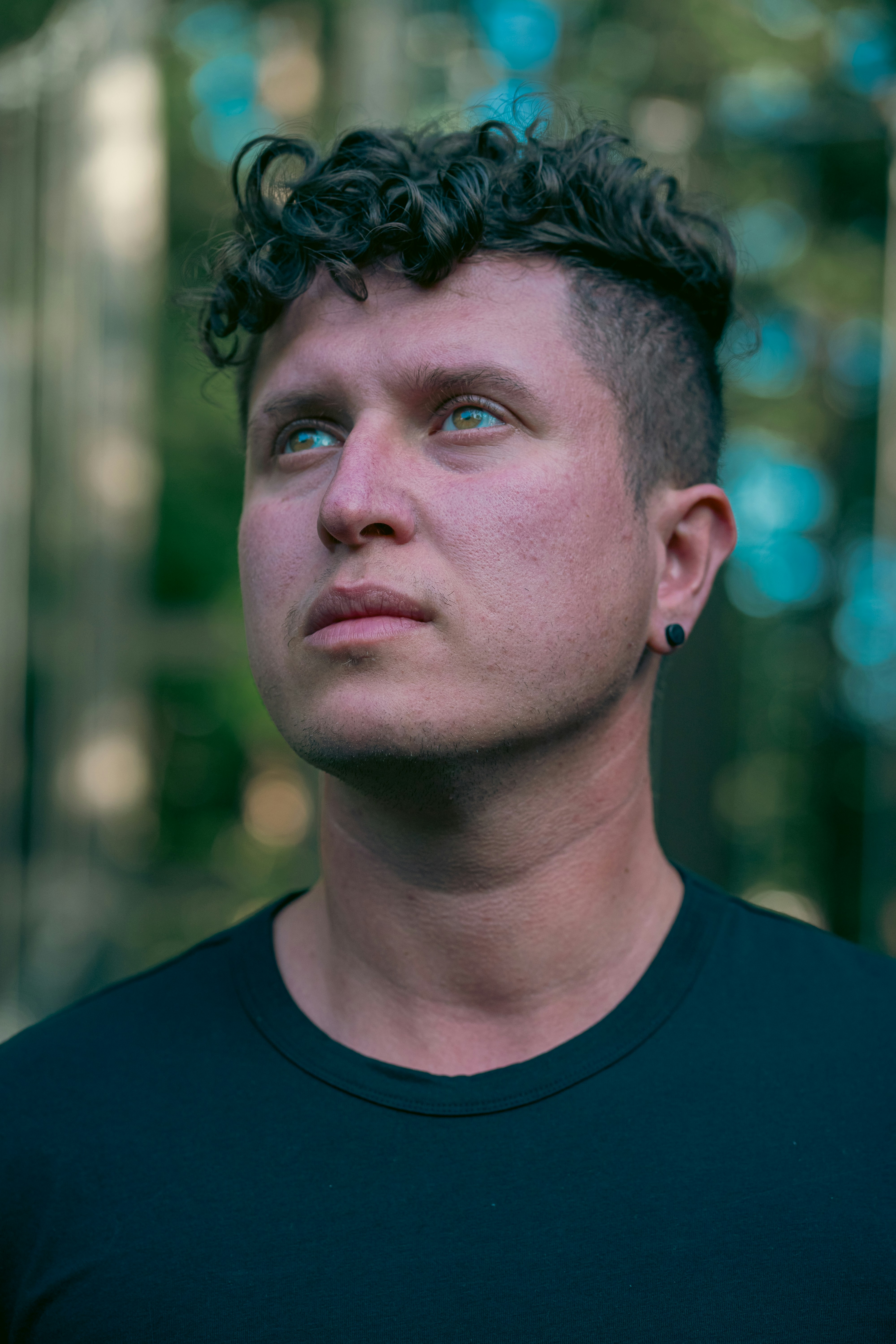 A man with curly hair and a black t-shirt looking upward outdoors