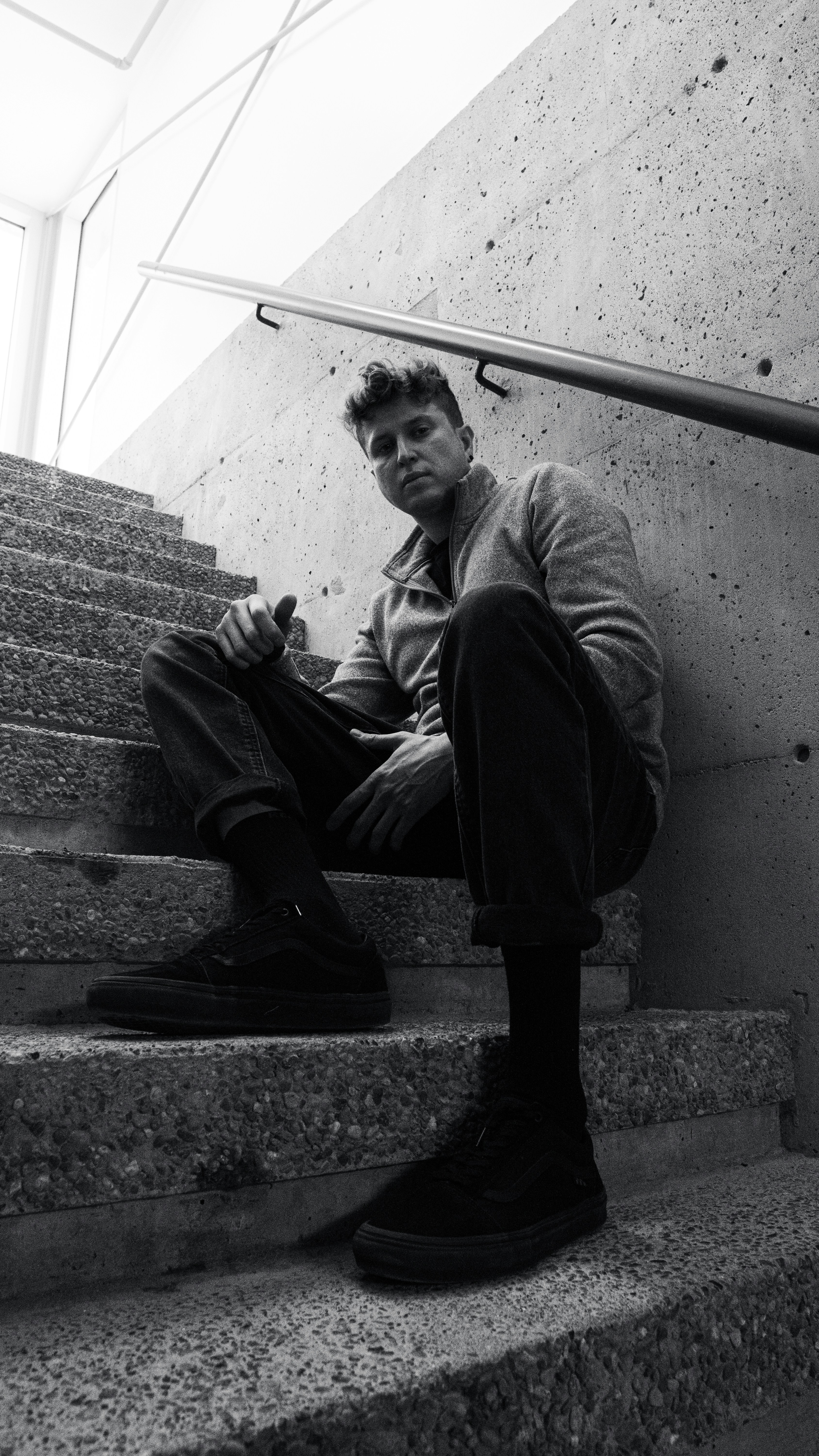 A man in a grey zip-up sweater sitting on concrete stairs