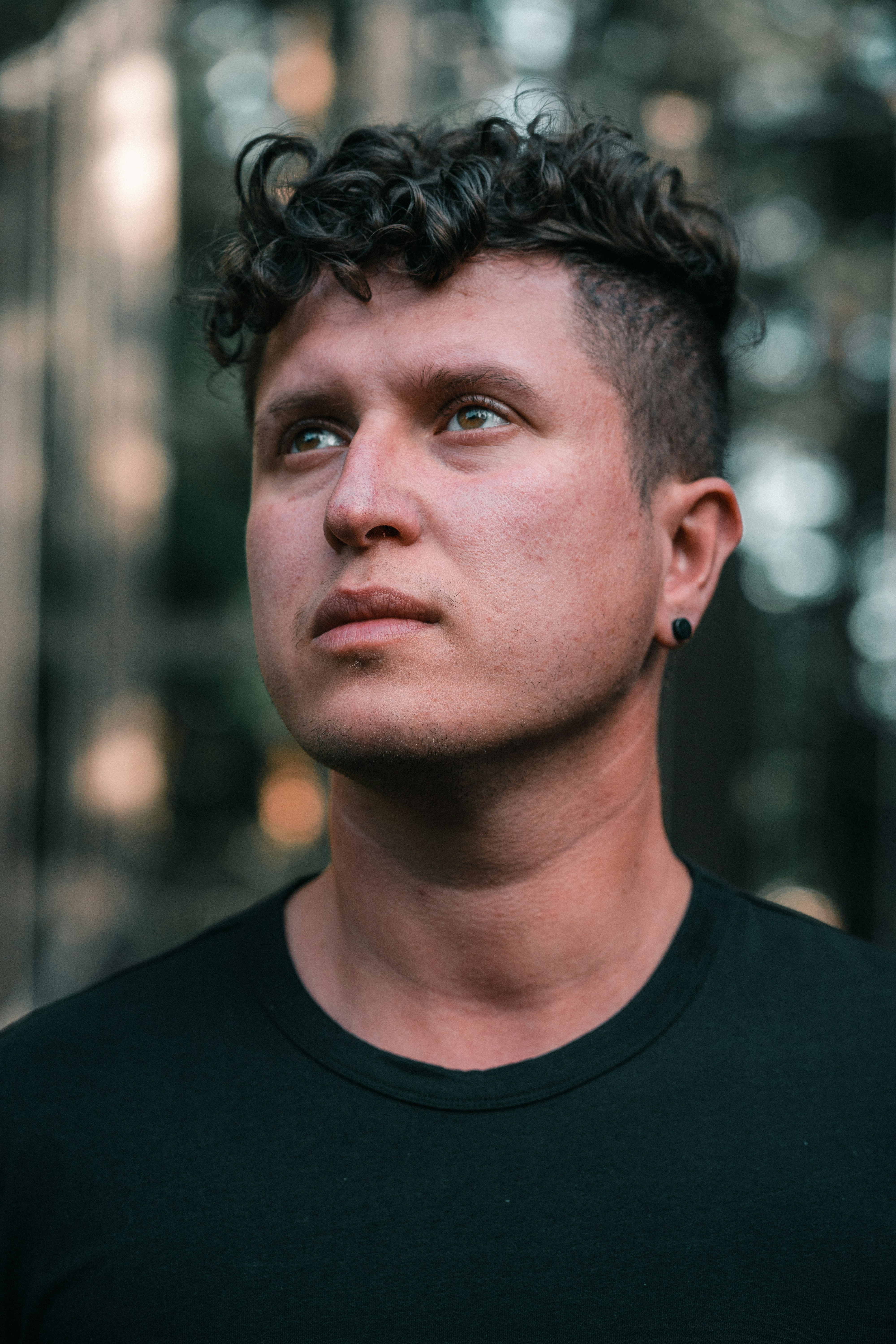 A man with curly dark hair and a black earring in a black shirt