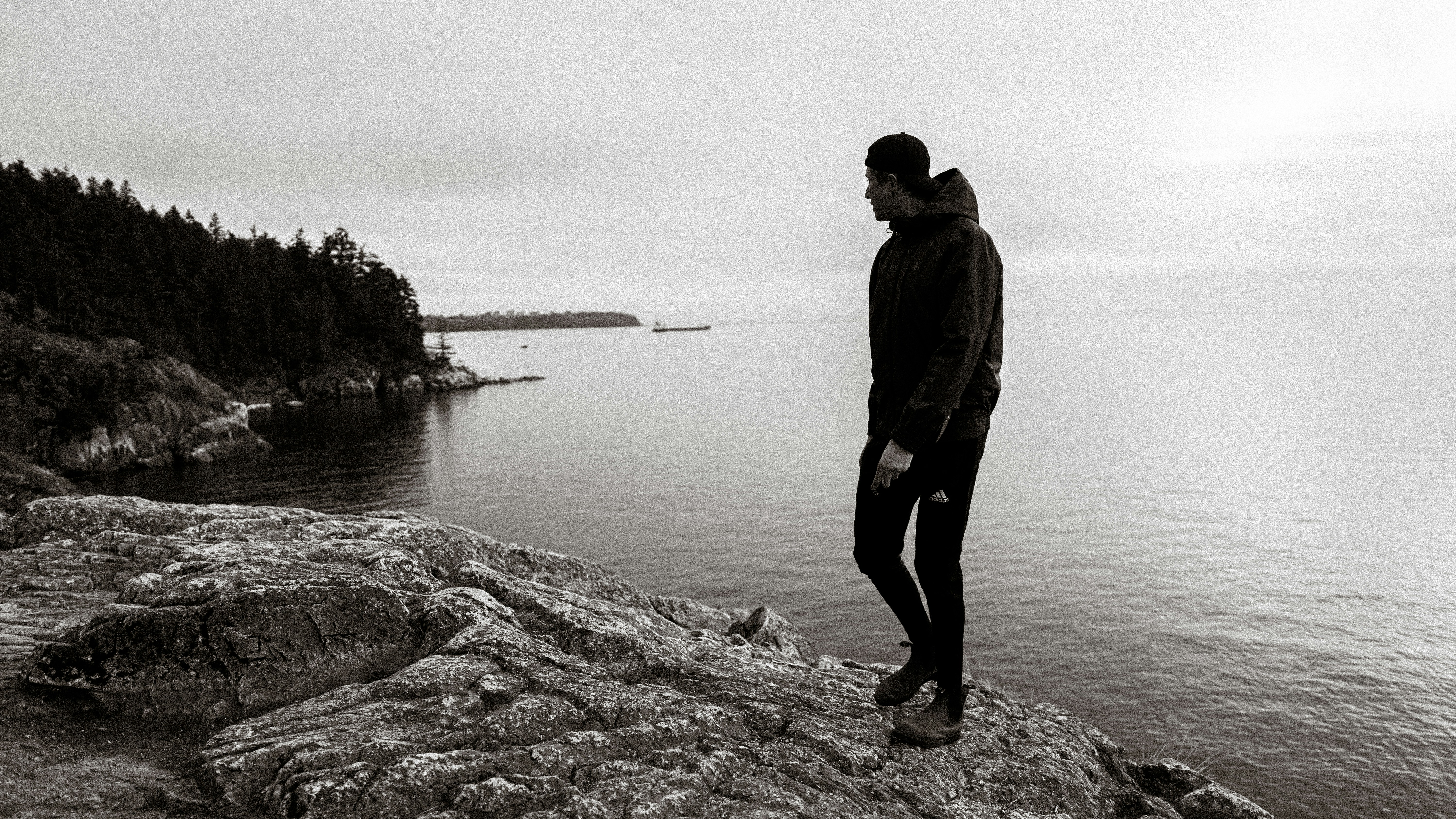 A person in a hooded jacket and cap on a rocky cliff overlooking water