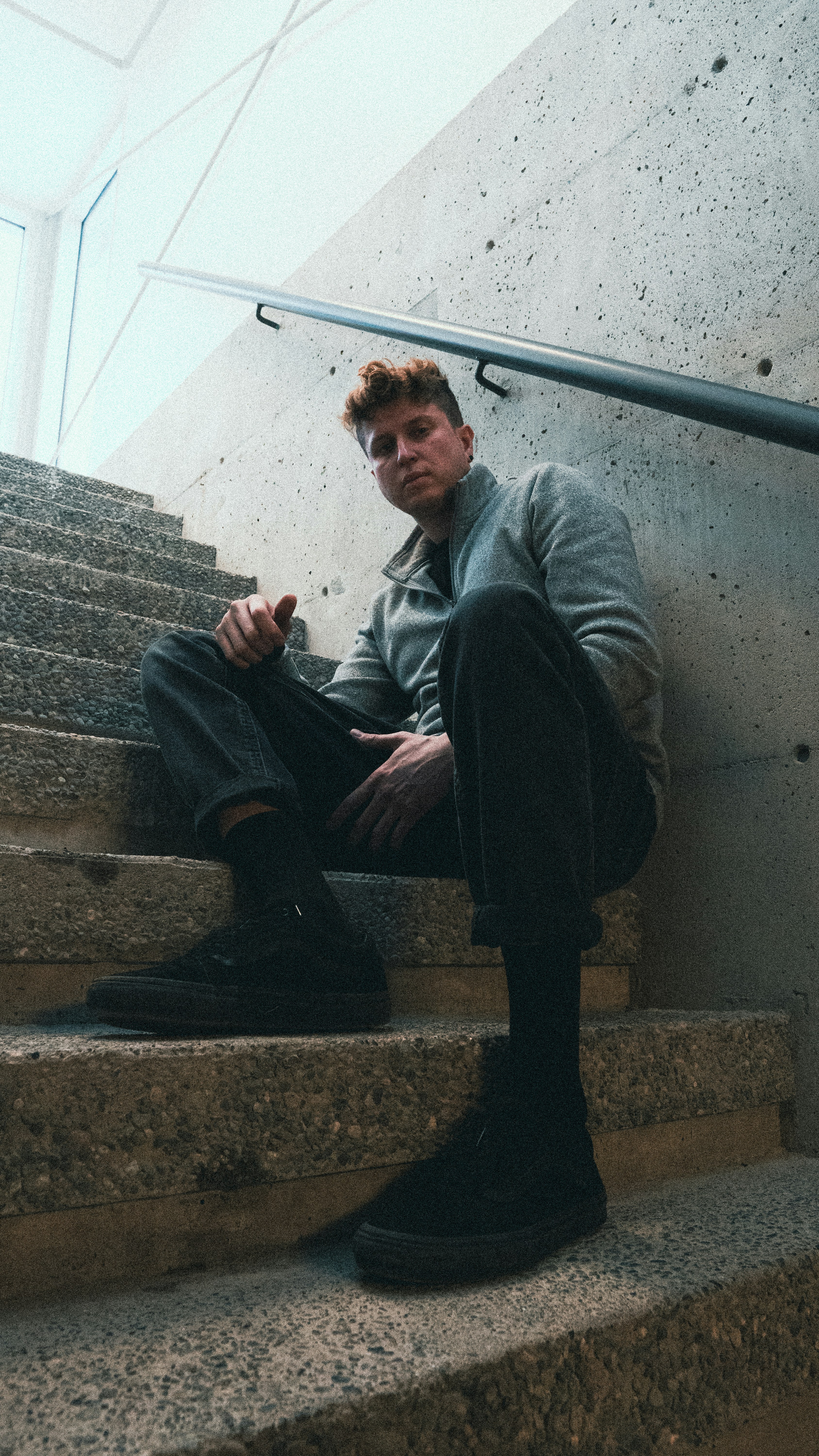 A person in a grey zip-up jacket on concrete stairs with a metal railing