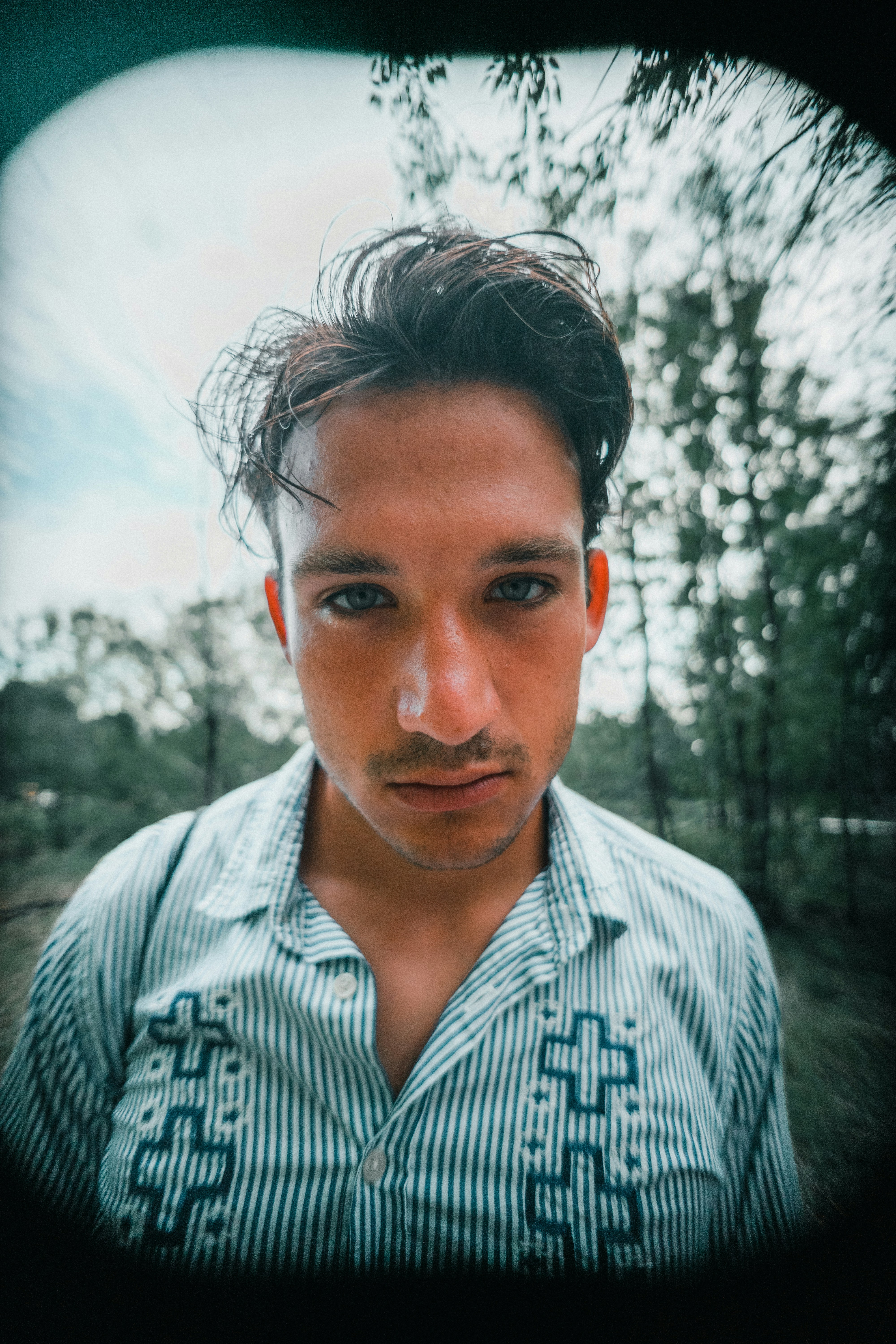 A man with dark hair in a striped shirt outdoors with a vignette effect