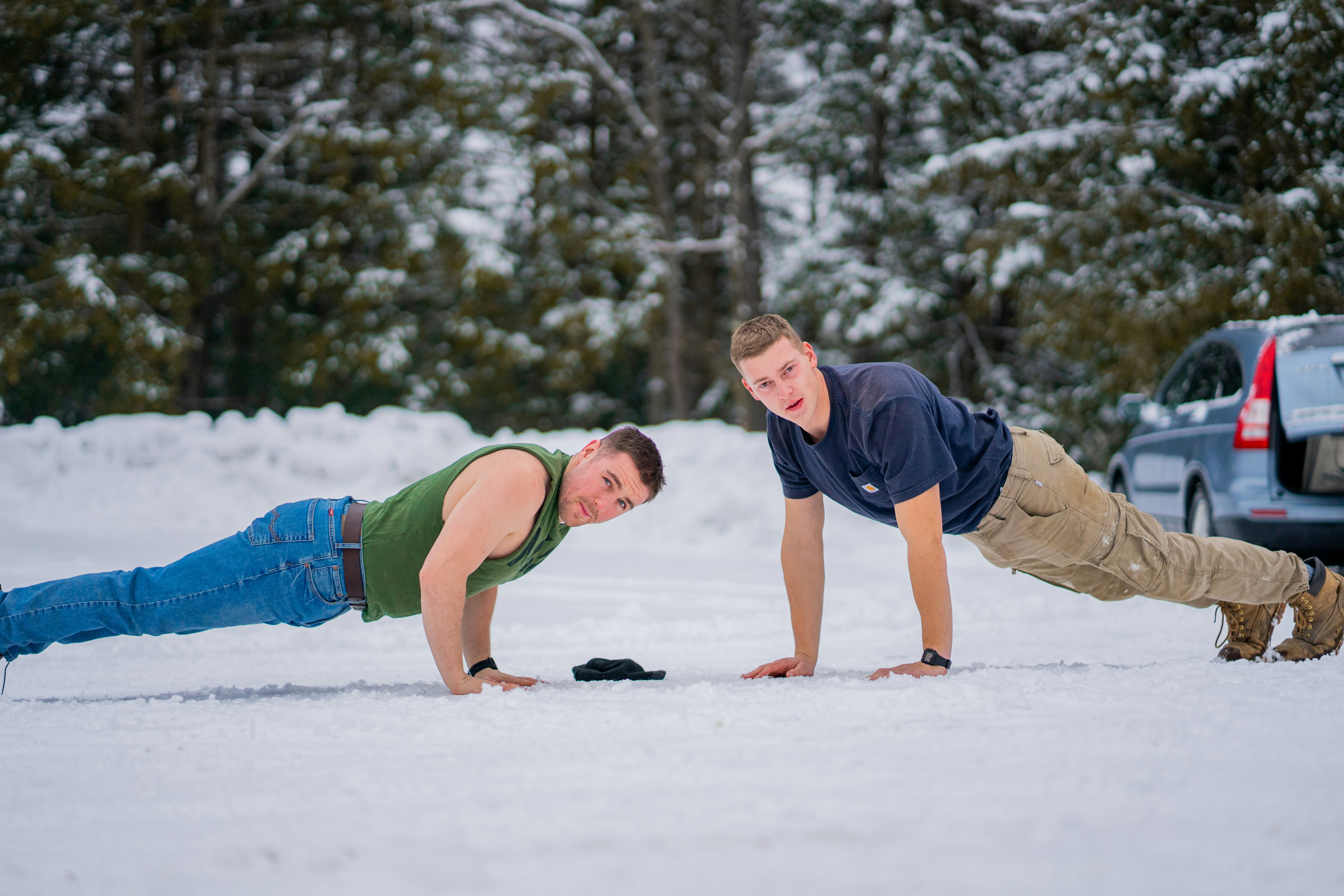 Two men doing pushups on a snow-covered ground in a forest
