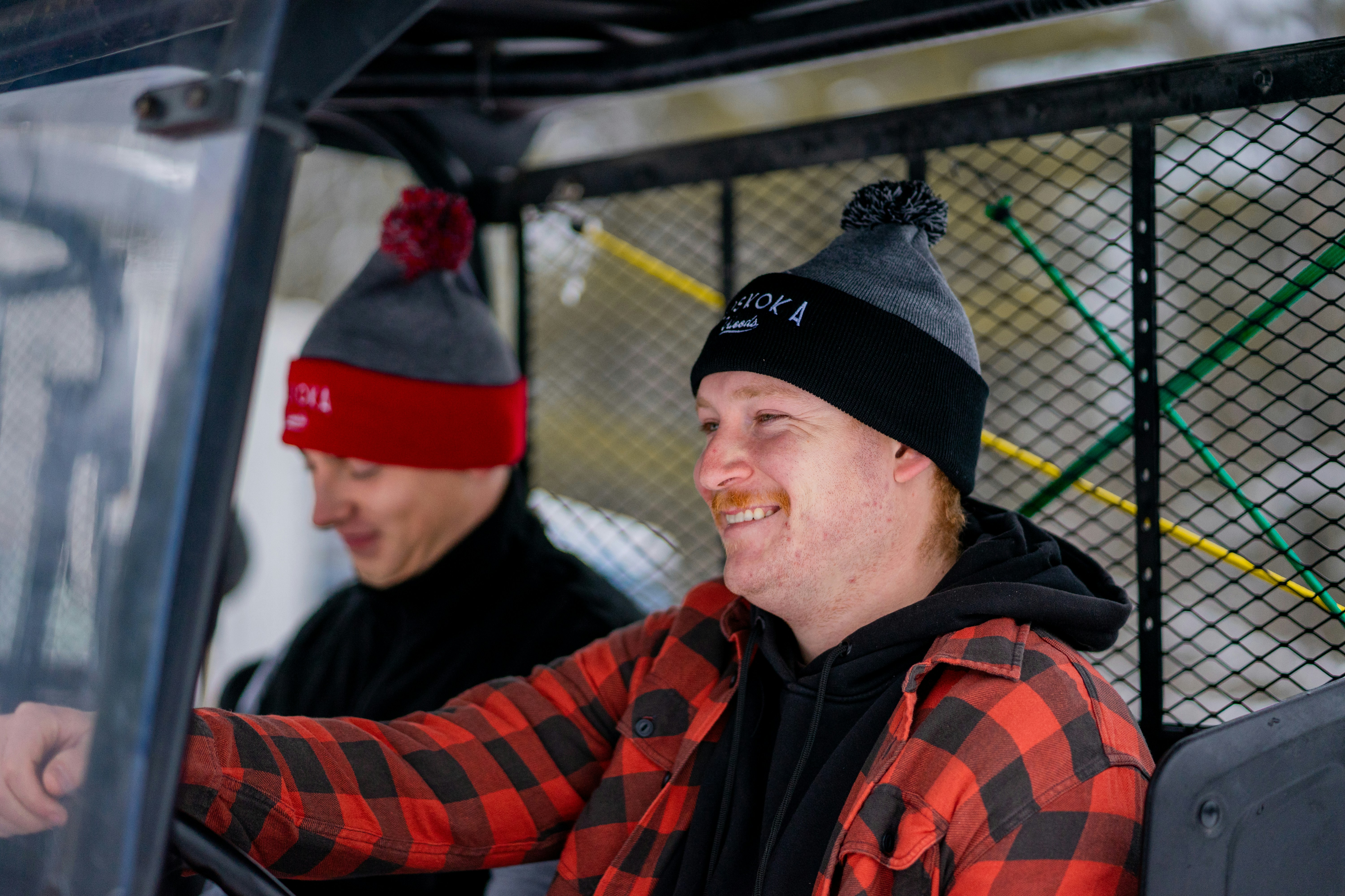 Two people in winter hats and plaid shirts inside a utility vehicle