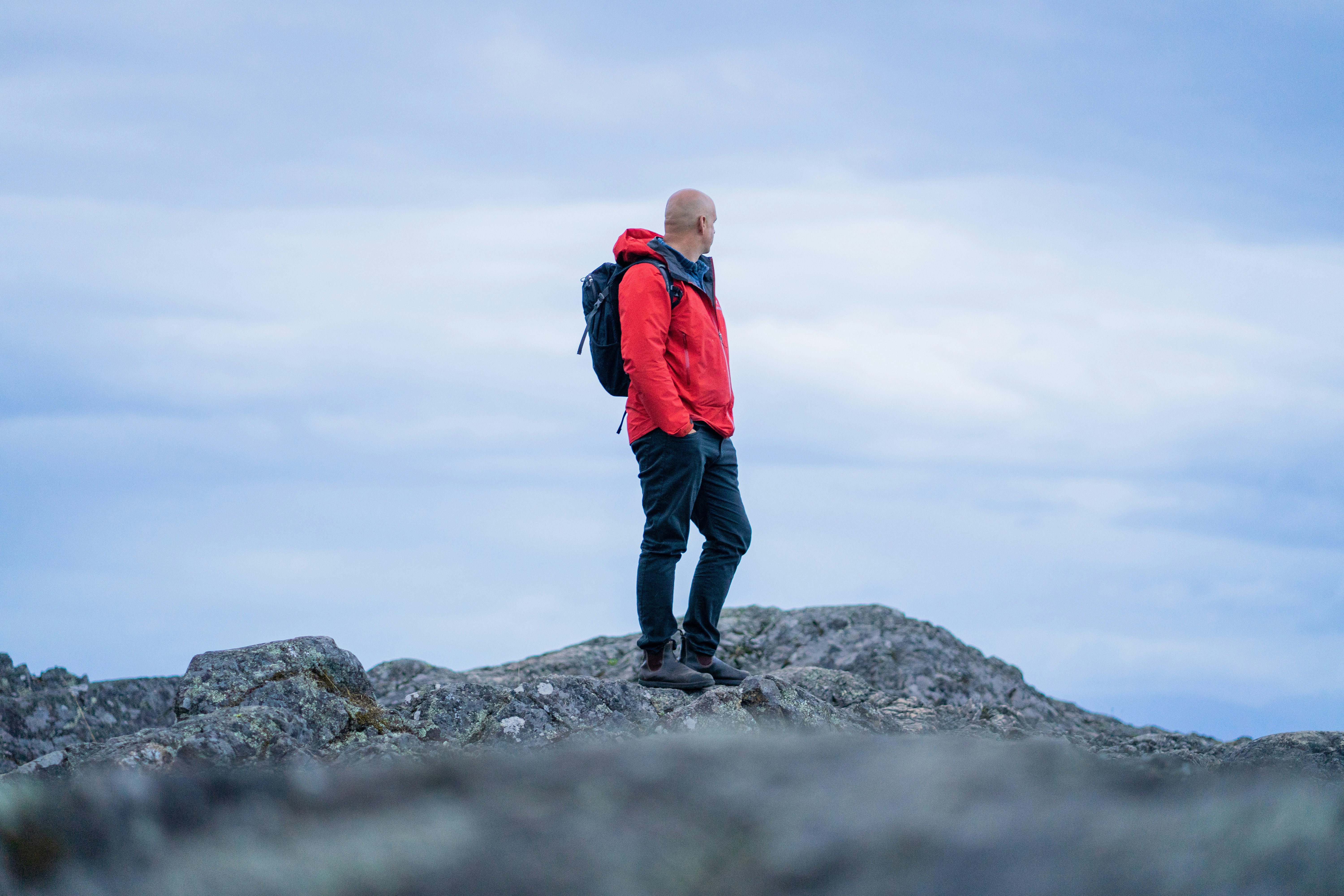 A man in a red jacket and backpack on a rocky mountain summit