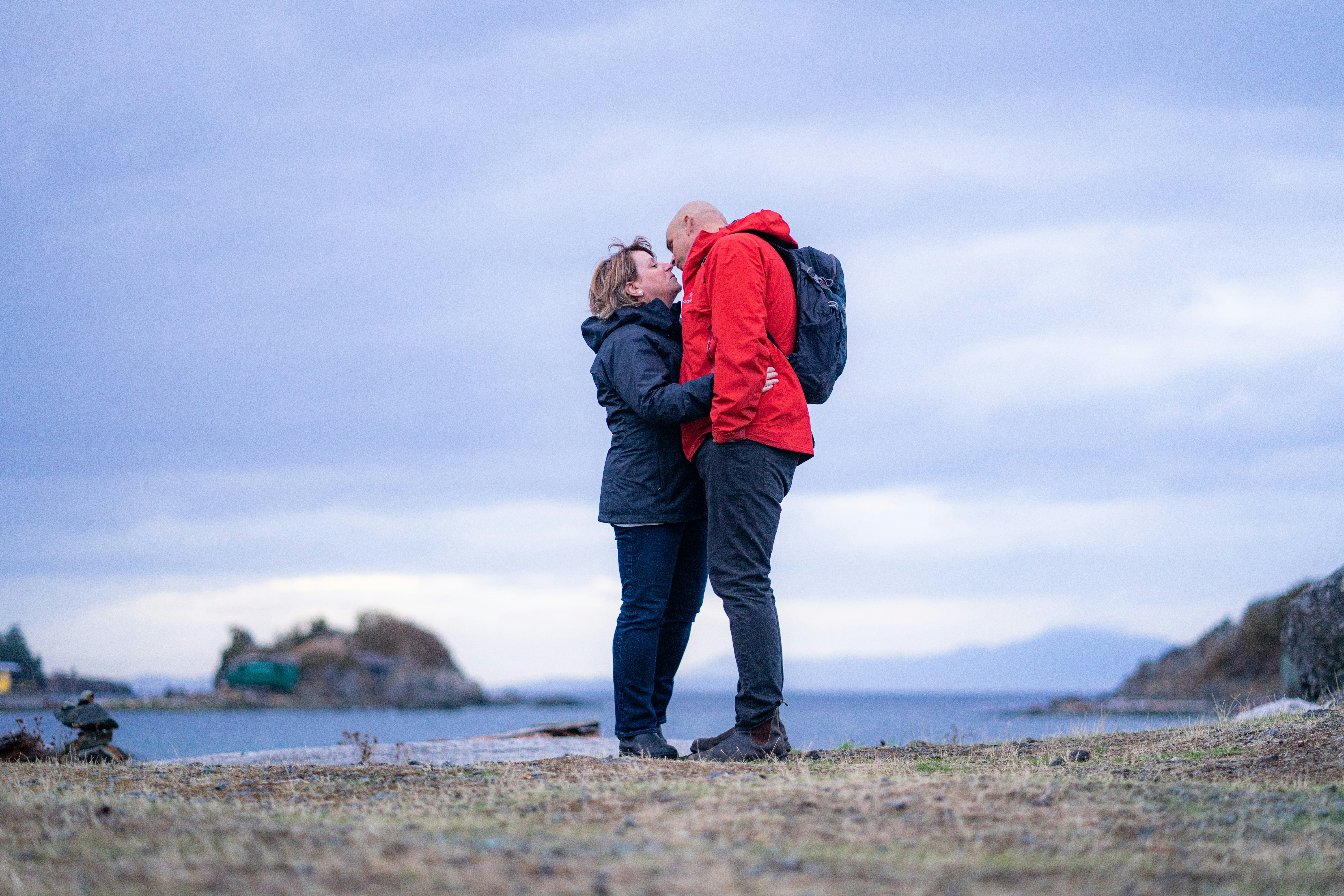 A woman and a man in jackets embracing on a rocky coastal shore