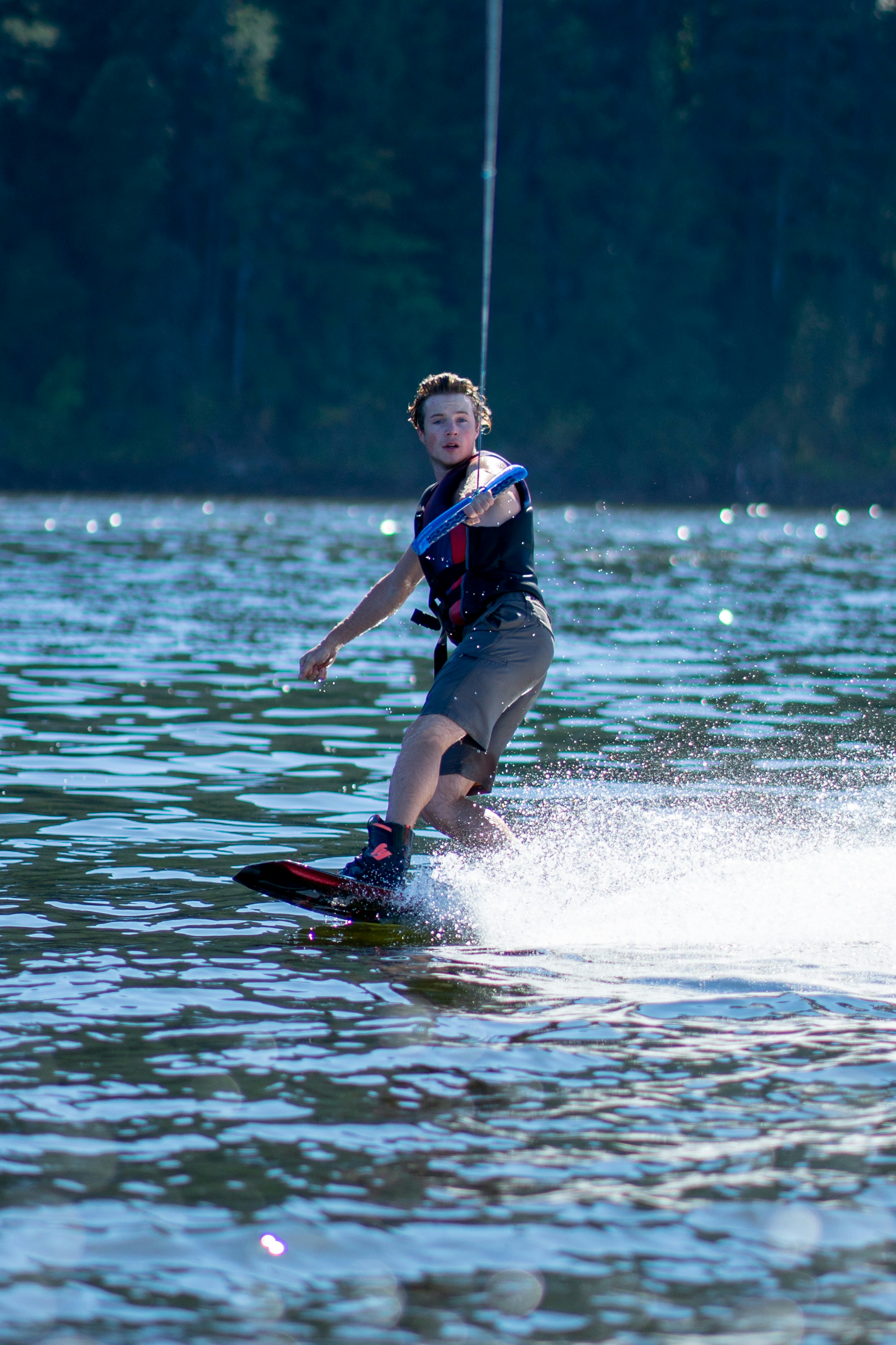A man wakeboarding on a lake, holding a tow rope in the sunlight