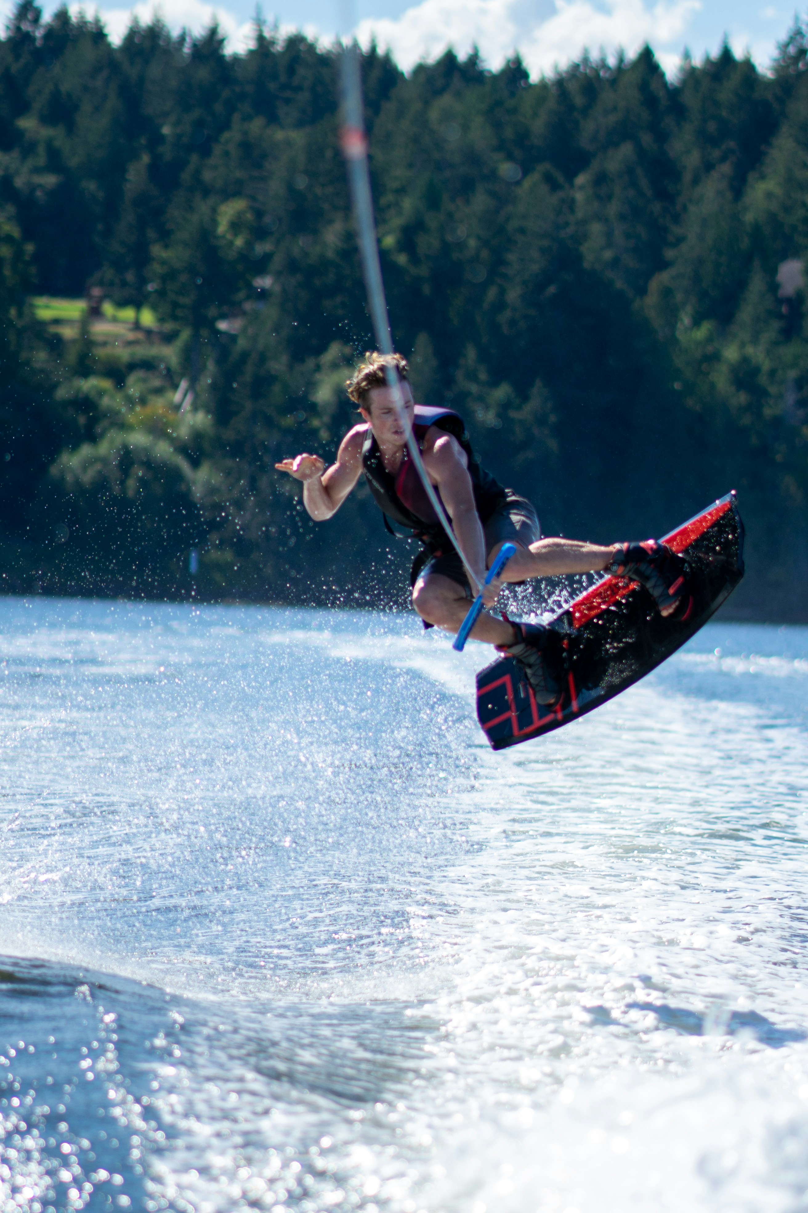 A man wakeboarding in the air above water with a forest in the background