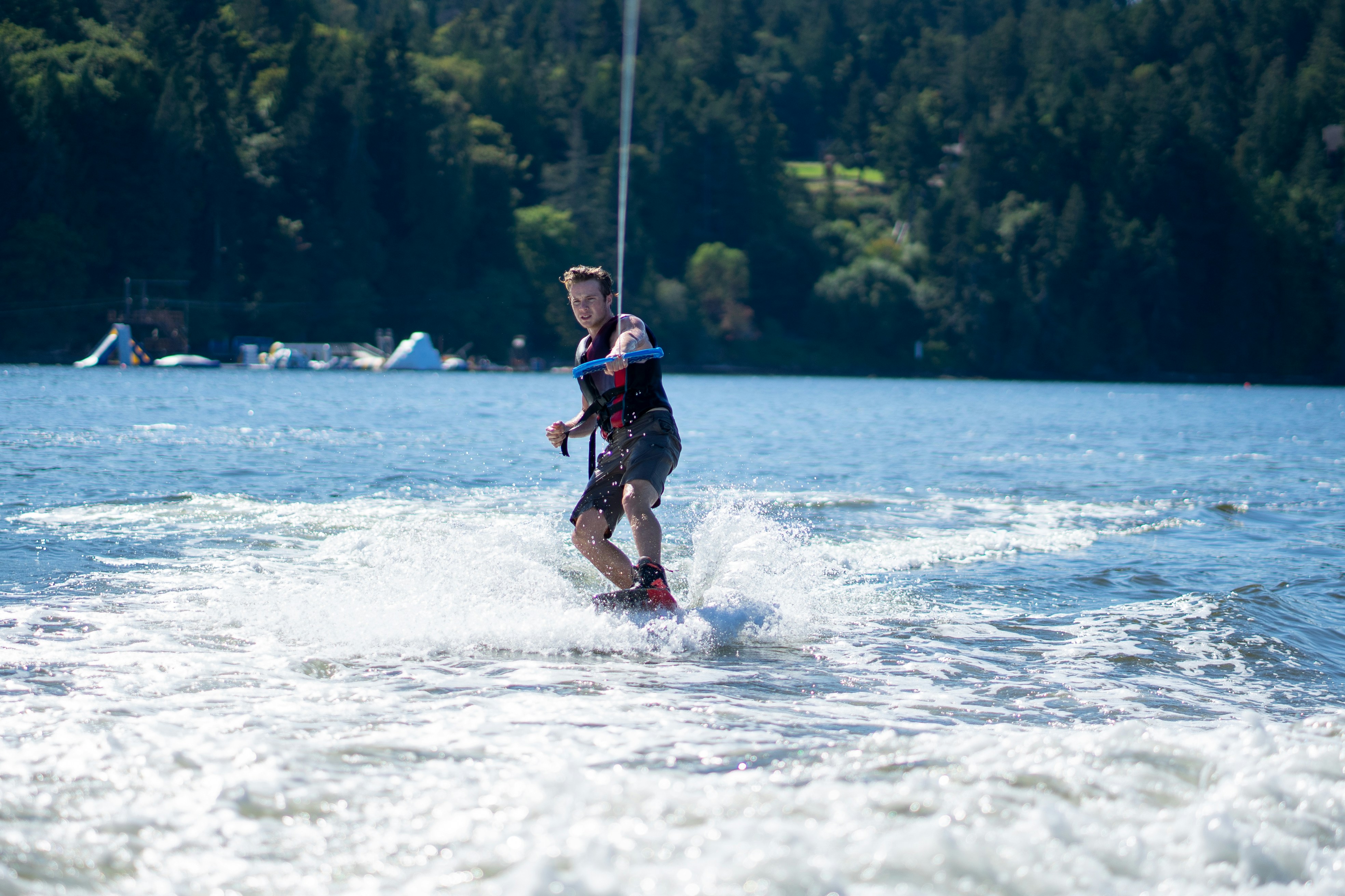 A man wakeboarding on a lake with a forested shoreline in the background