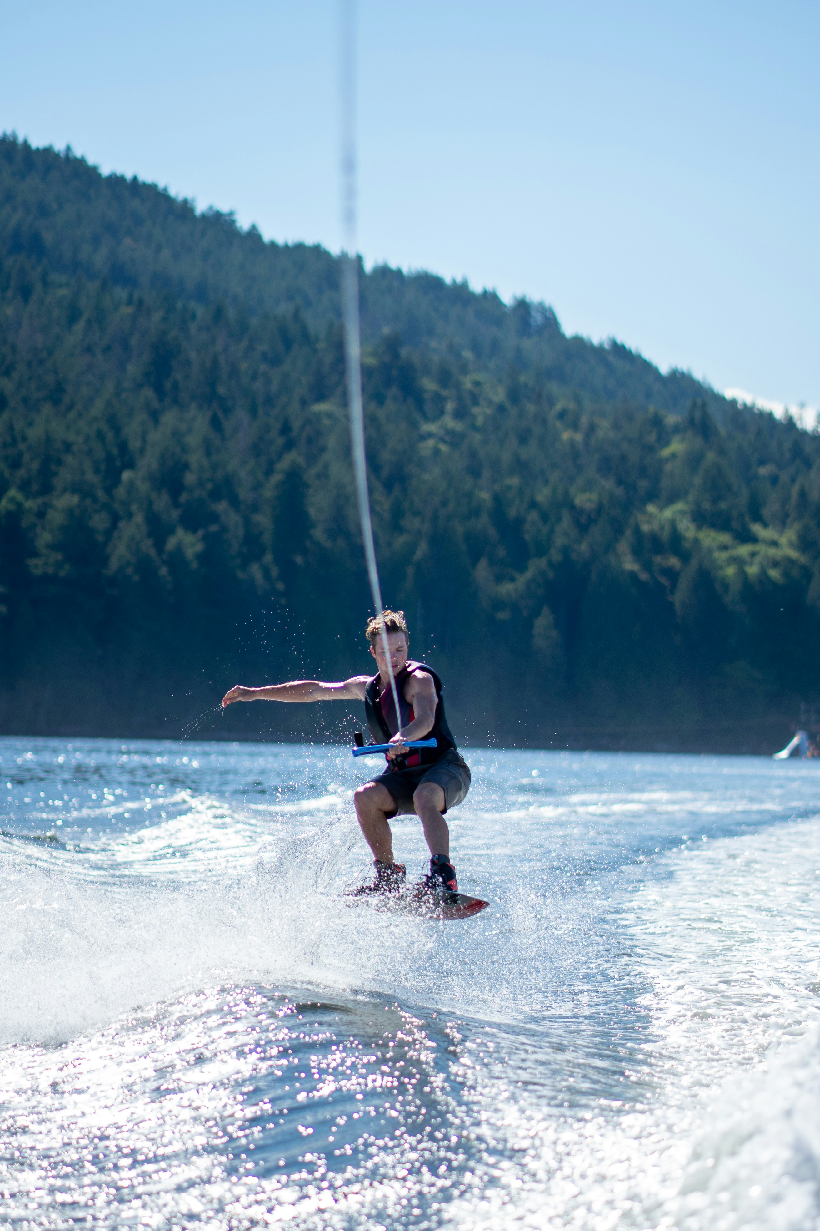 A man wakeboarding on a lake with a forested mountain in the background