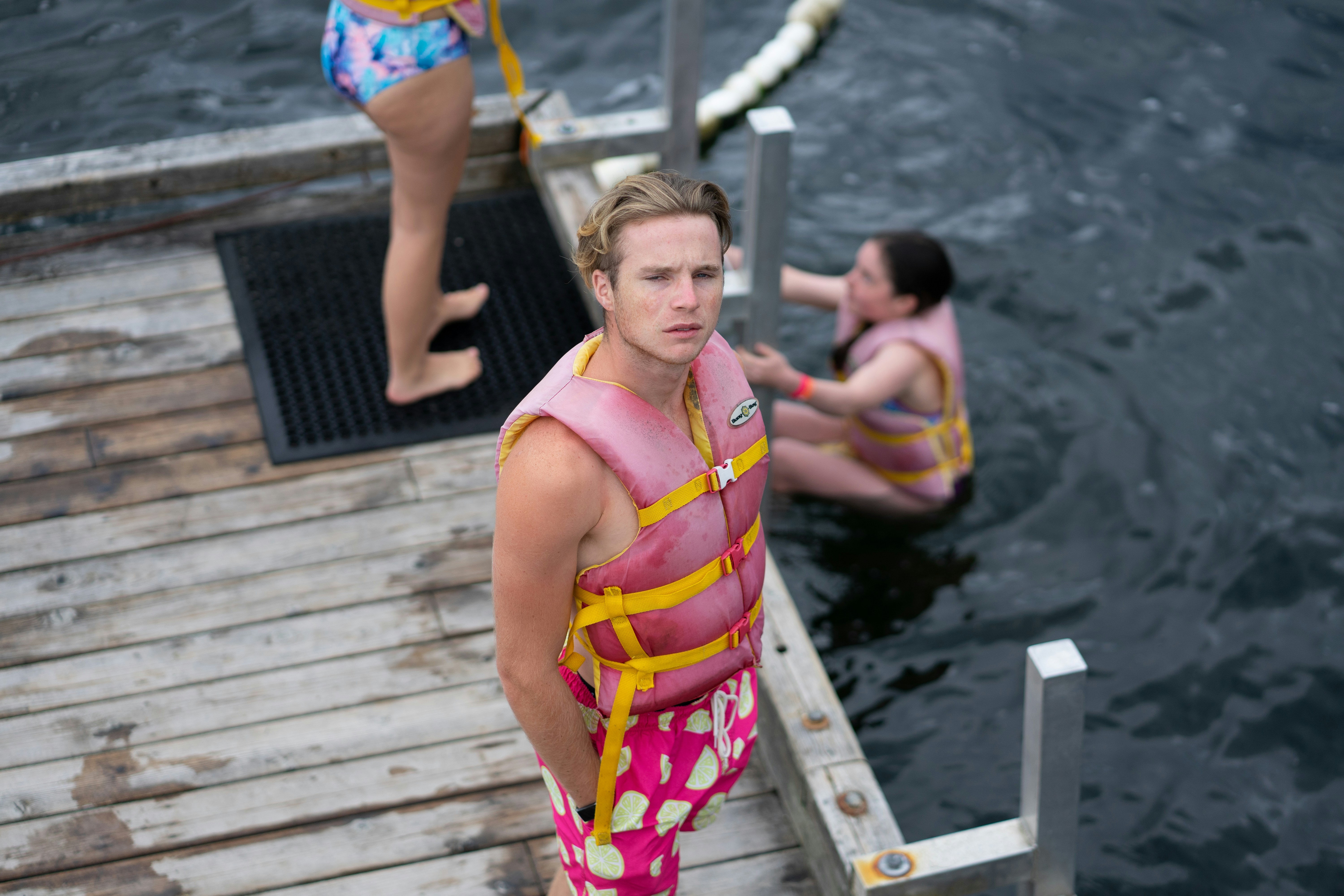 A man in a pink life vest and patterned shorts on a wooden dock