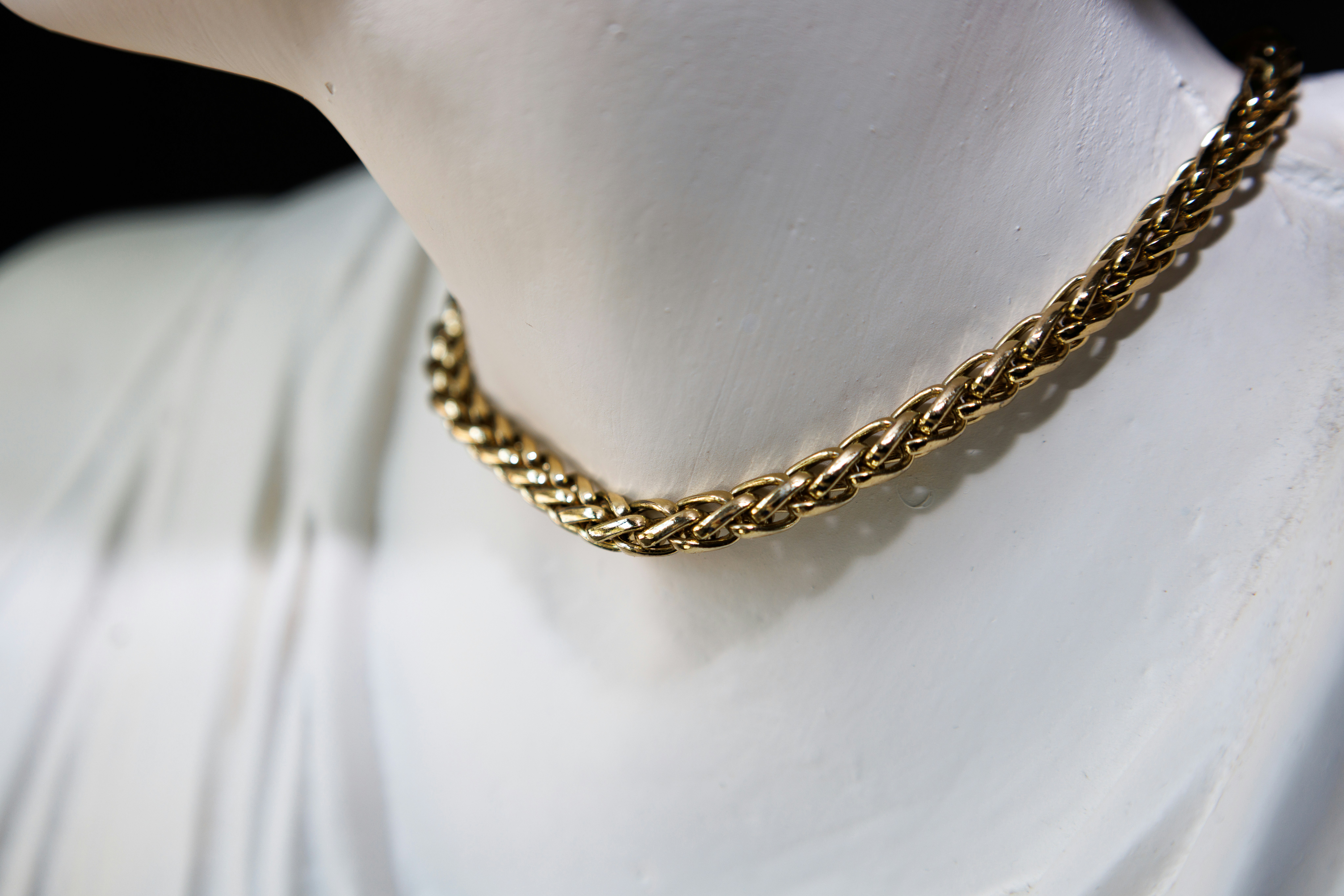 A thick gold chain necklace around the neck of a white plaster bust