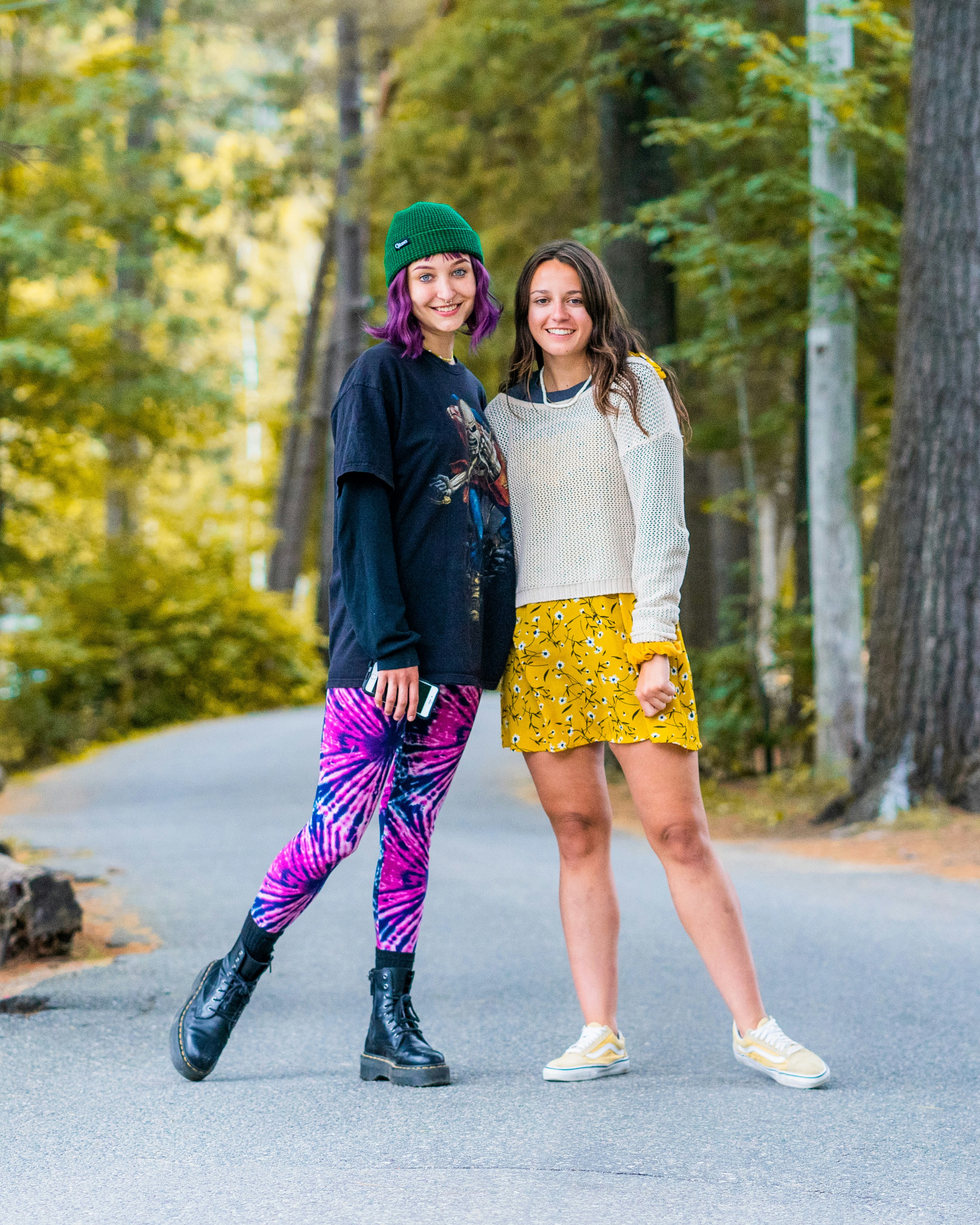 Two young women standing together on a paved path in a wooded park