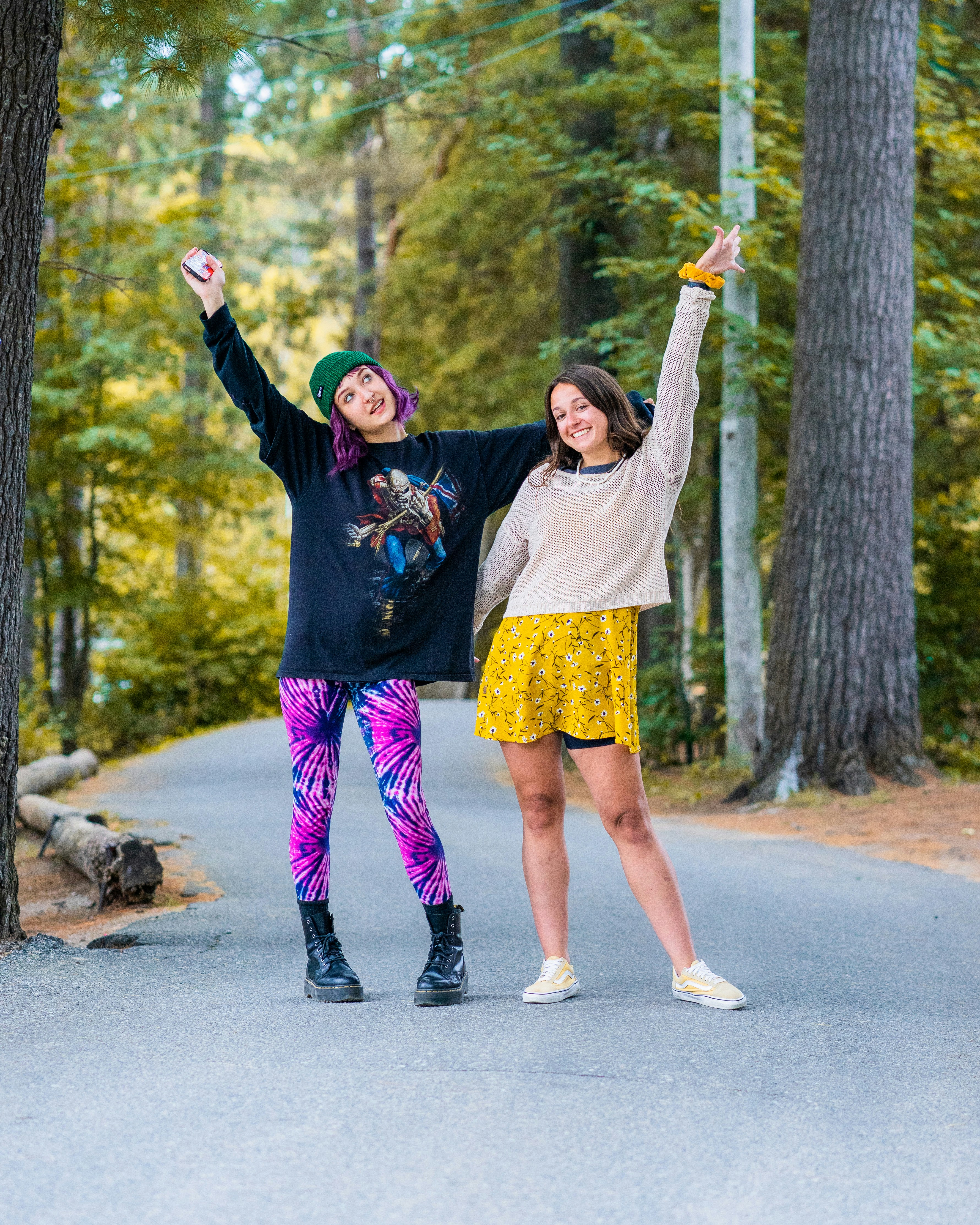 Two women with arms raised on a paved path through a forest