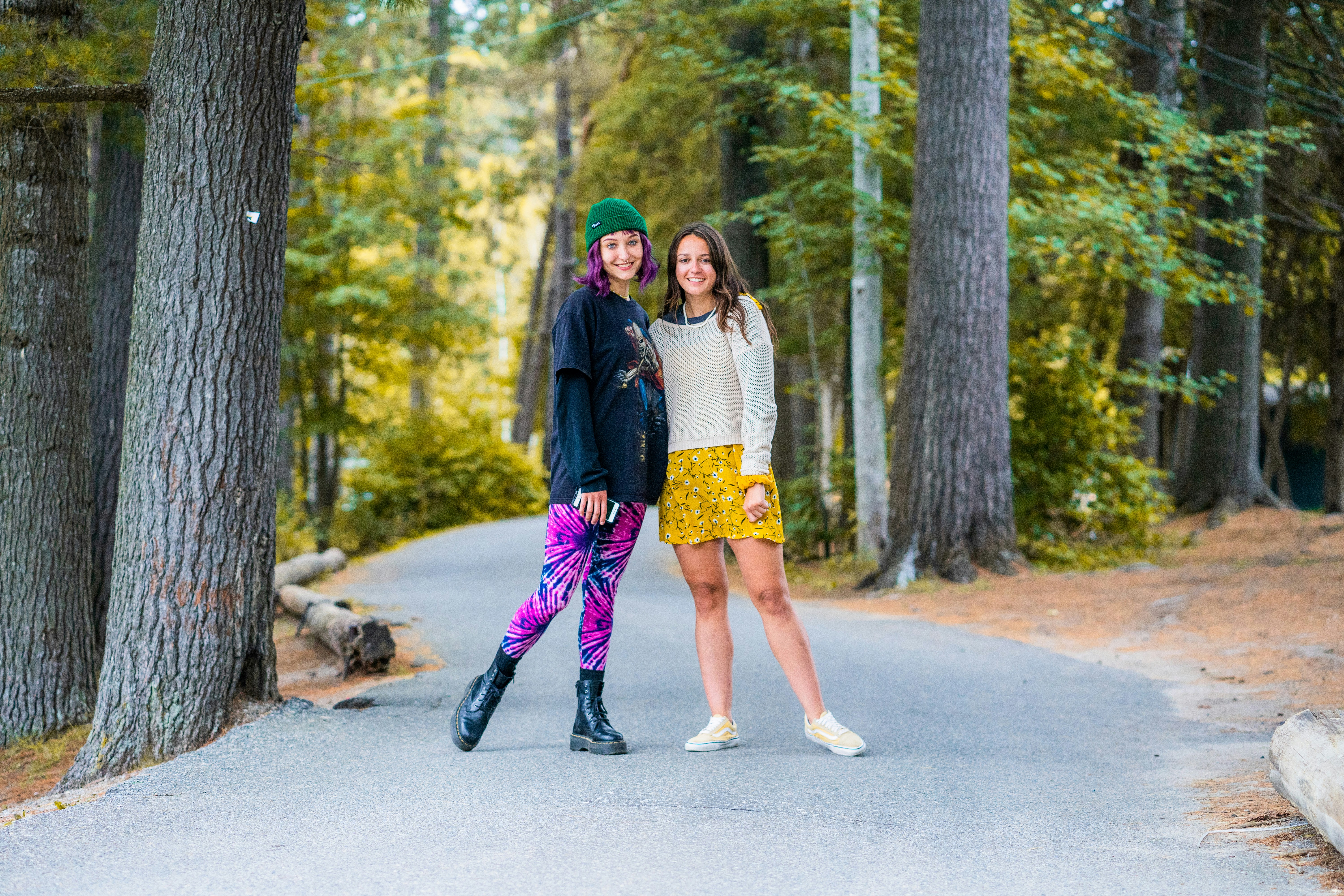 Two young women standing on a paved path in a forest
