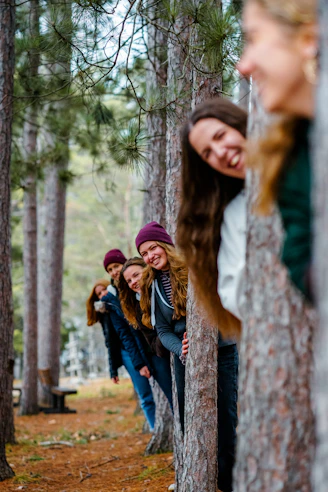 A line of people peeking from behind pine trees in a forest