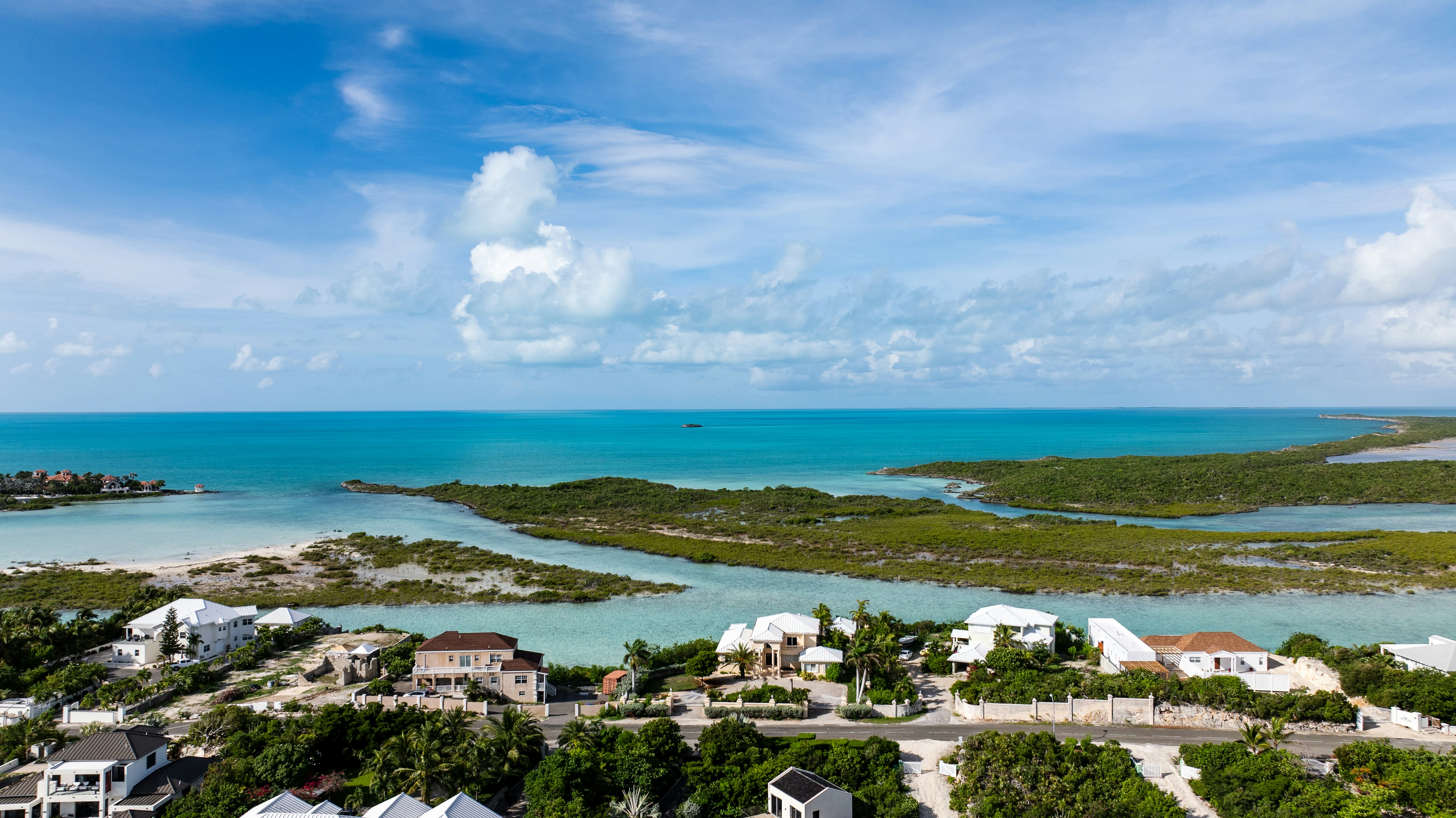Aerial view of coastal houses along a turquoise bay with lush green mangroves