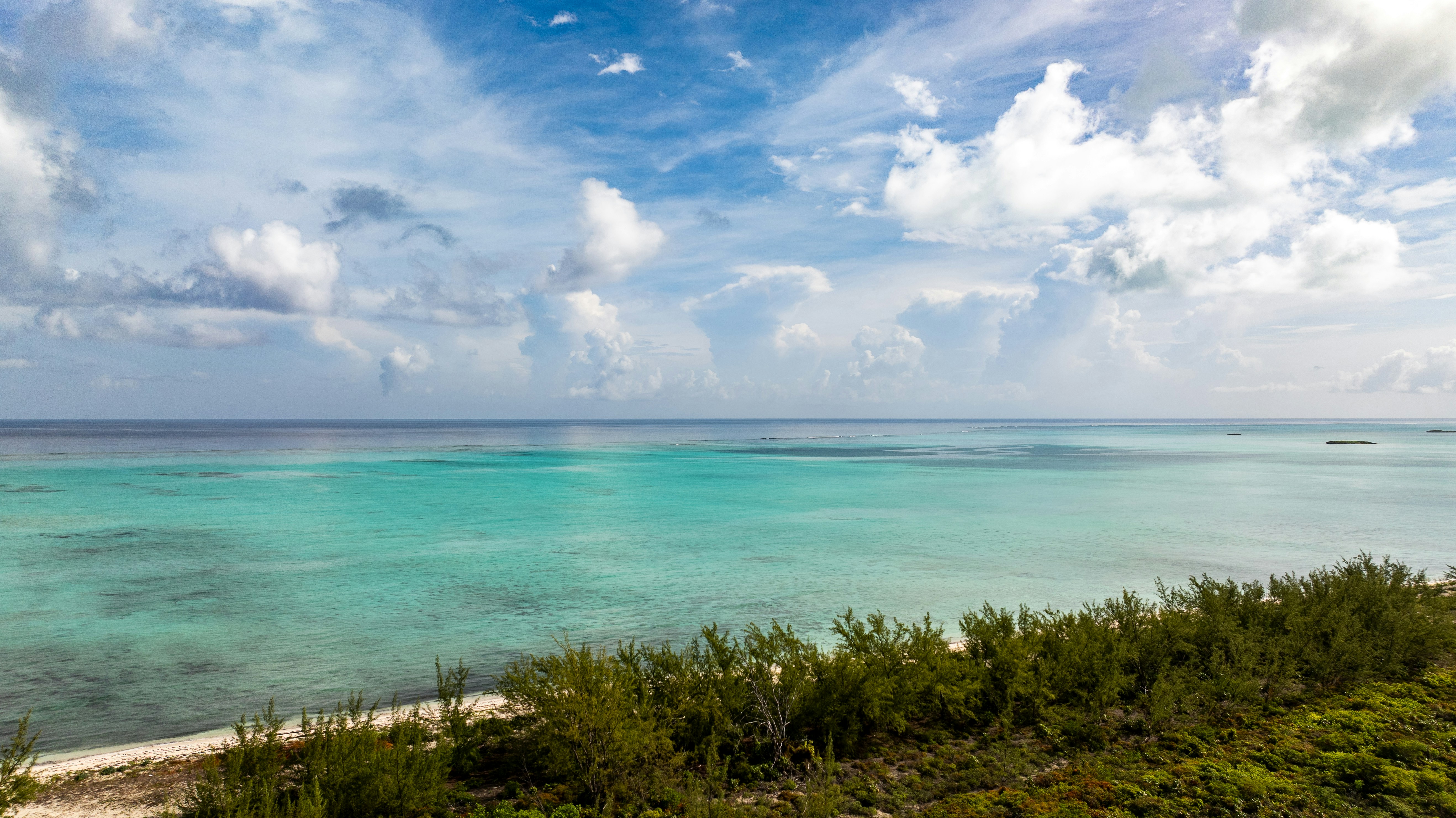 Turquoise water along a sandy beach with green trees under a cloudy sky