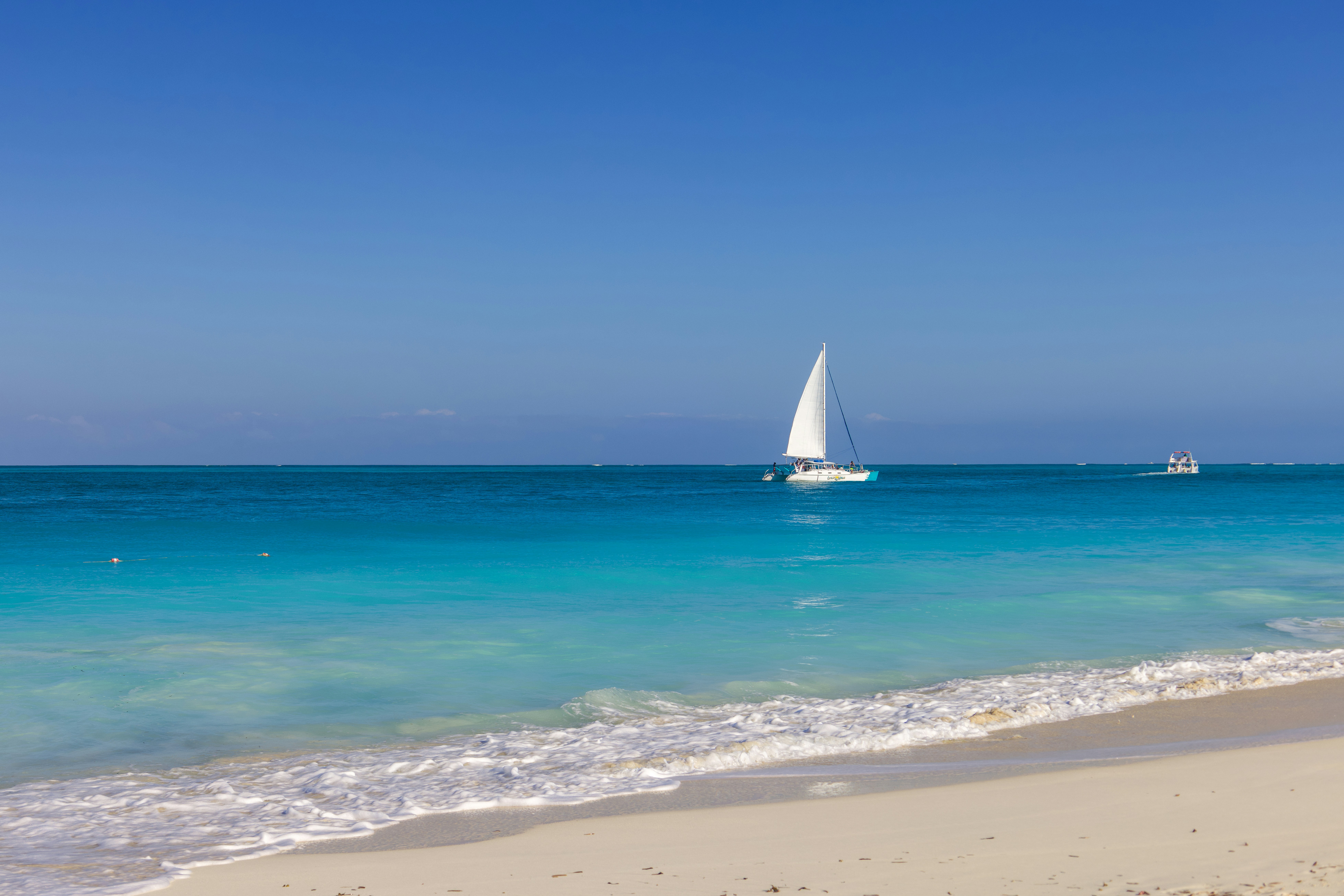White sailboat on ocean with sandy beach