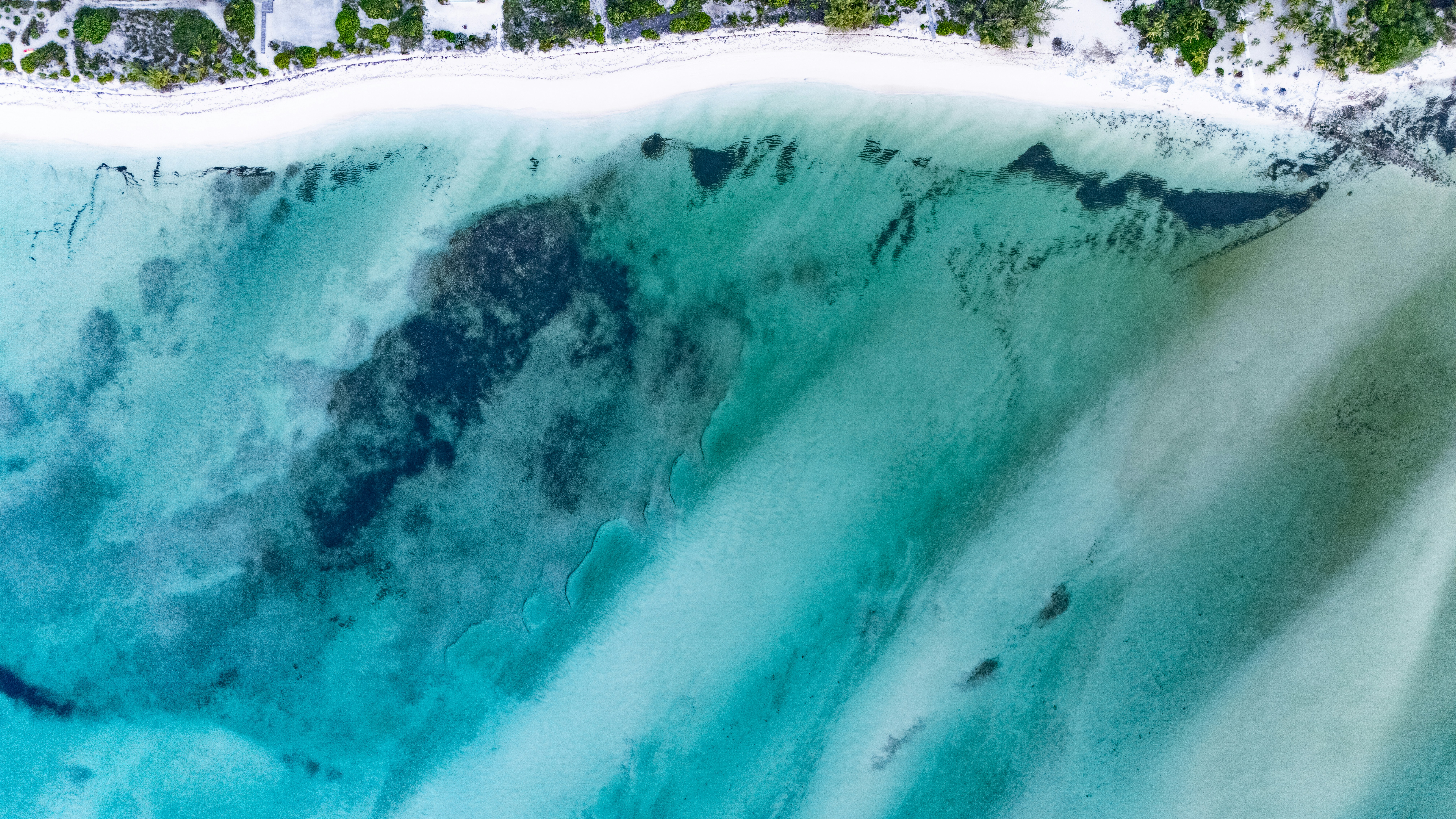 An aerial view of a white sandy beach meeting turquoise ocean water