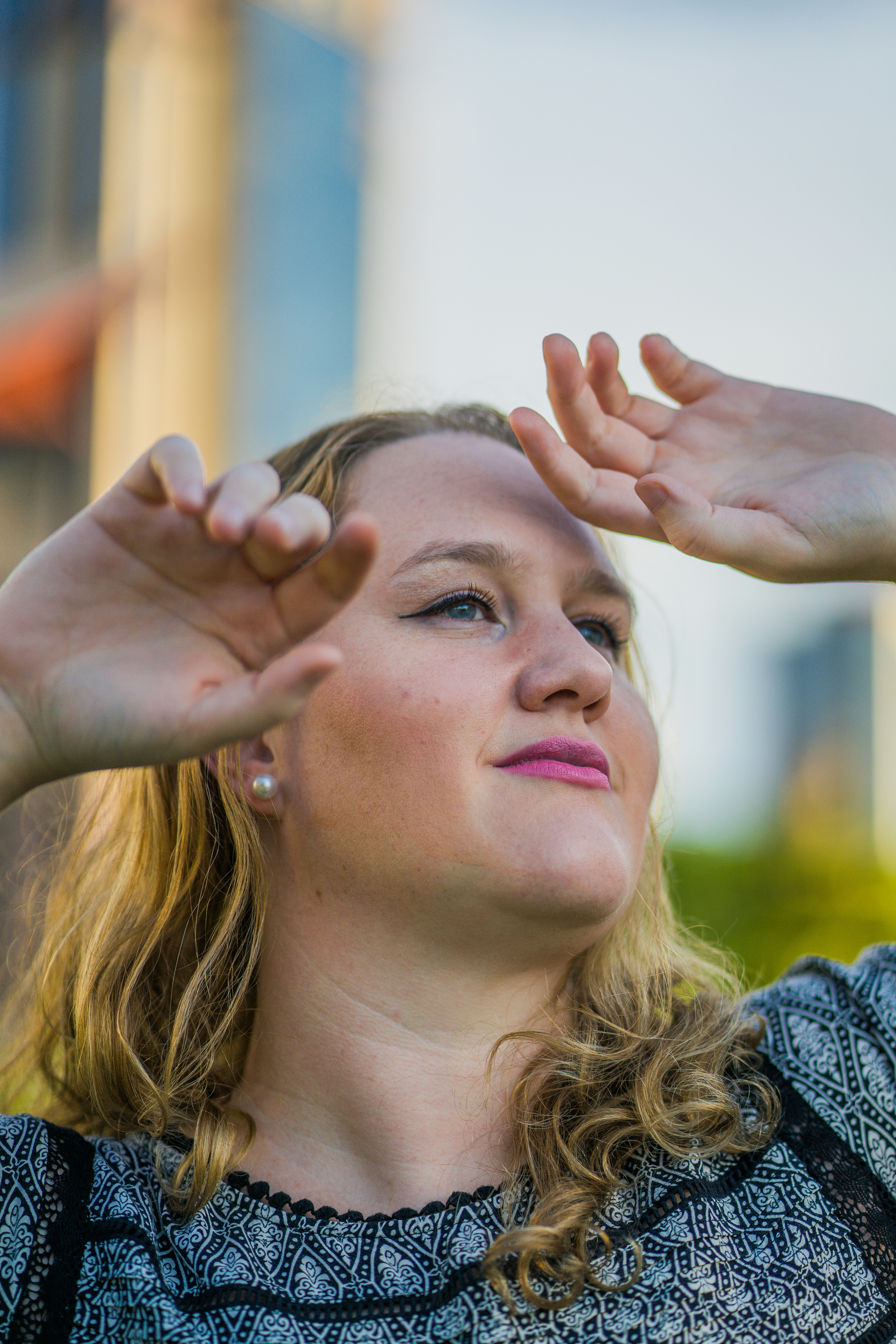 A woman with blonde hair shielding her eyes from the sun outdoors