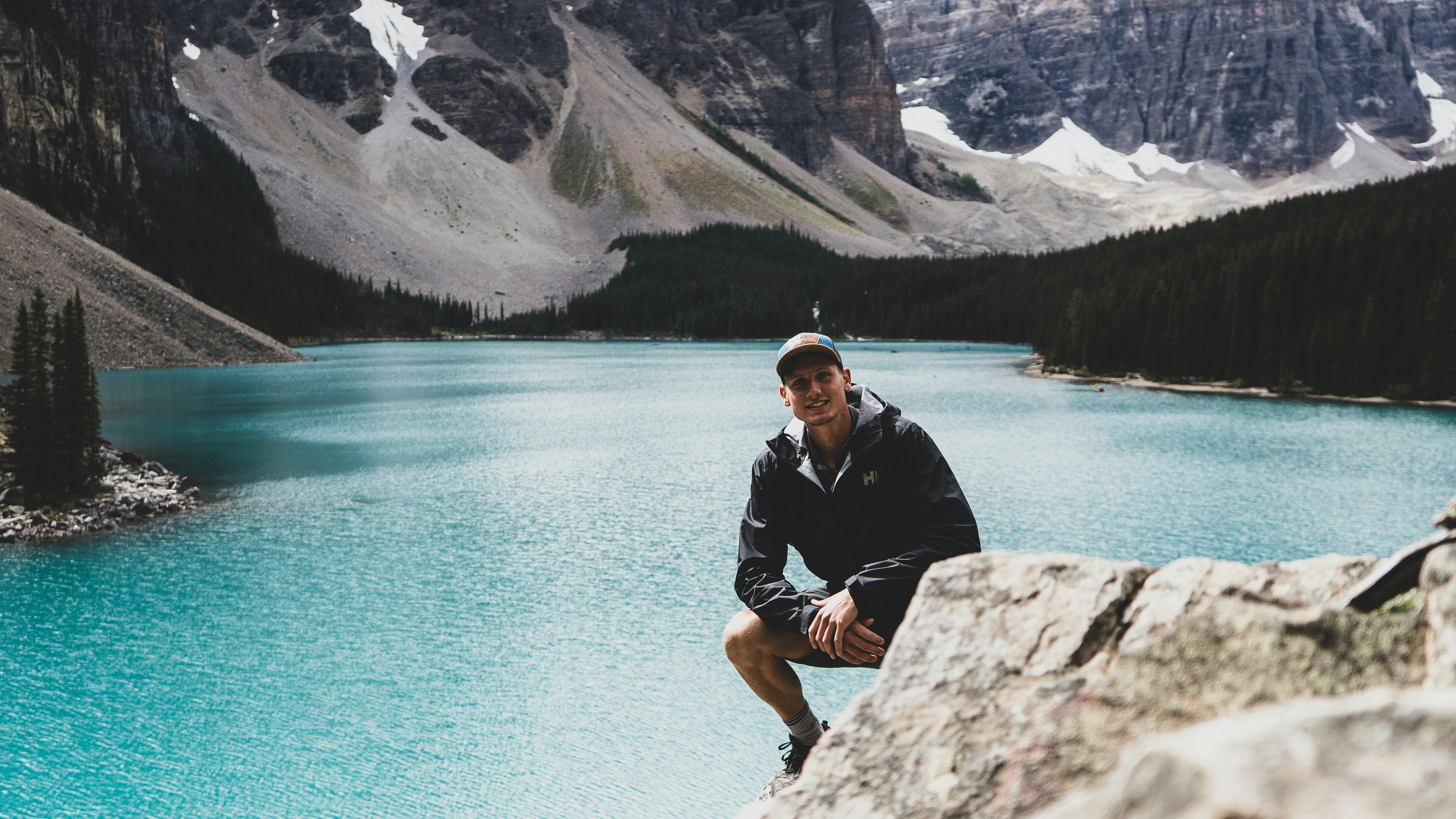 A man crouching on a rock above a turquoise alpine lake