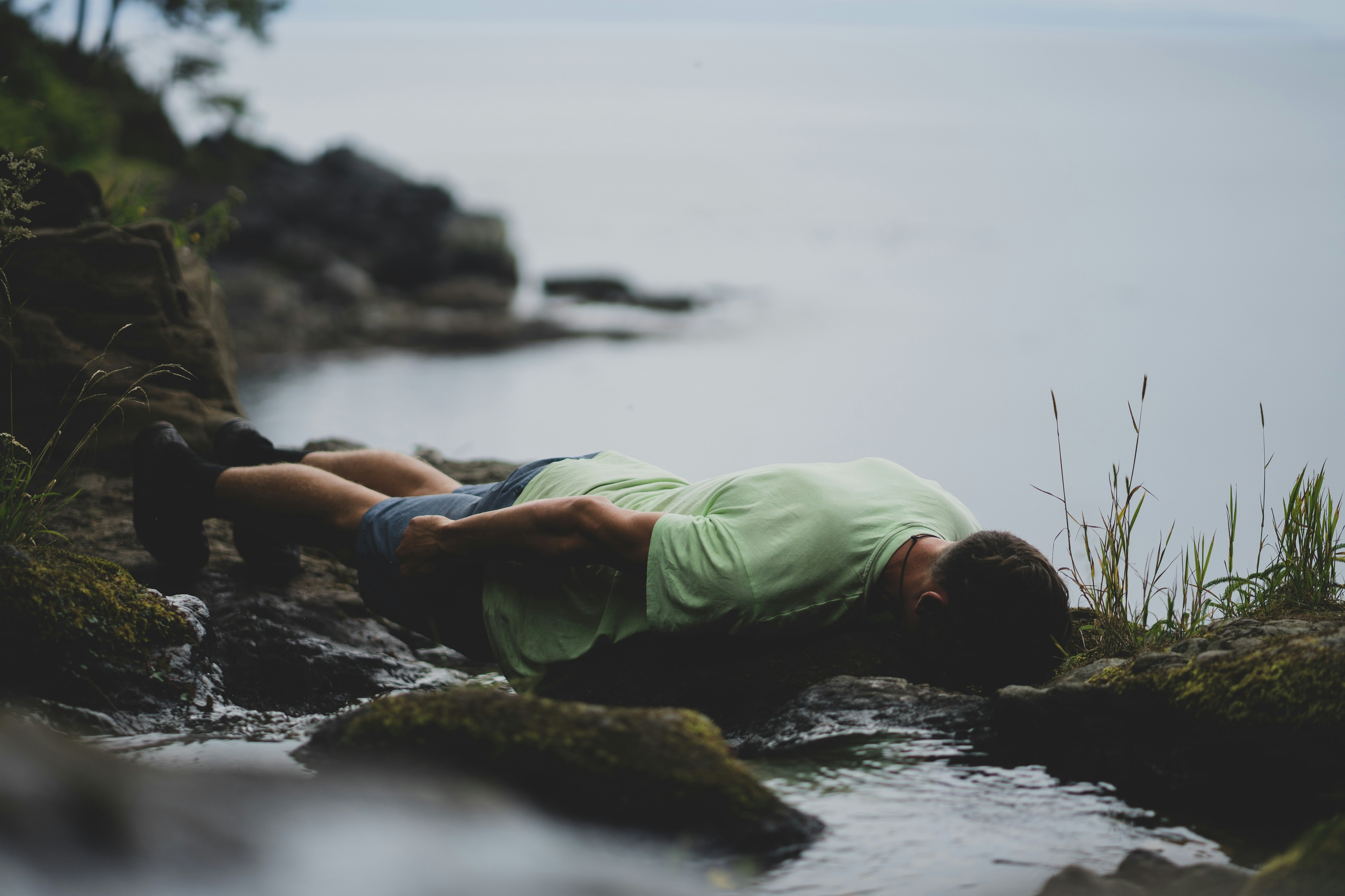 A person in a light green shirt lying on mossy rocks by water