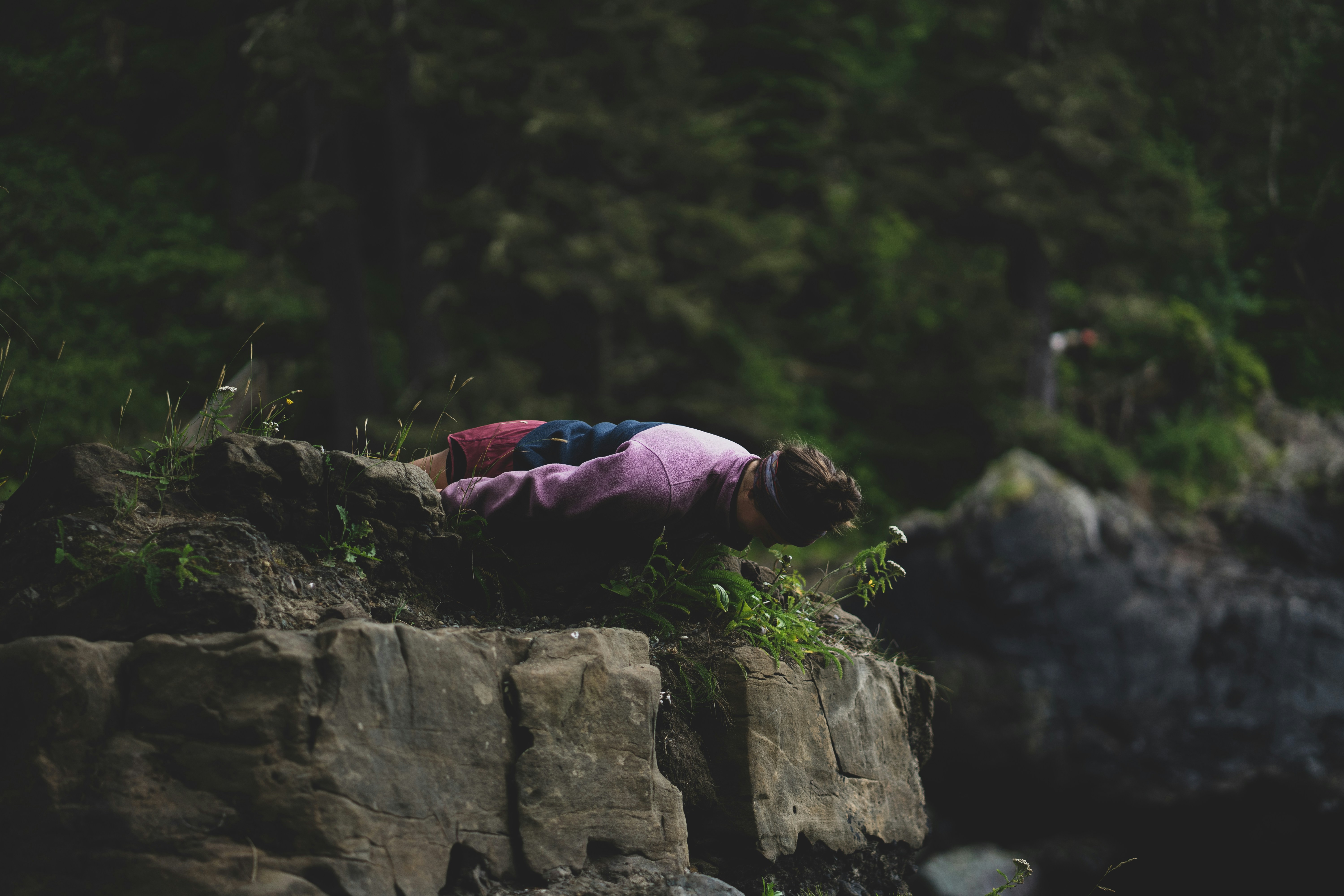 A person in a pink sweatshirt leaning over a rocky cliff edge