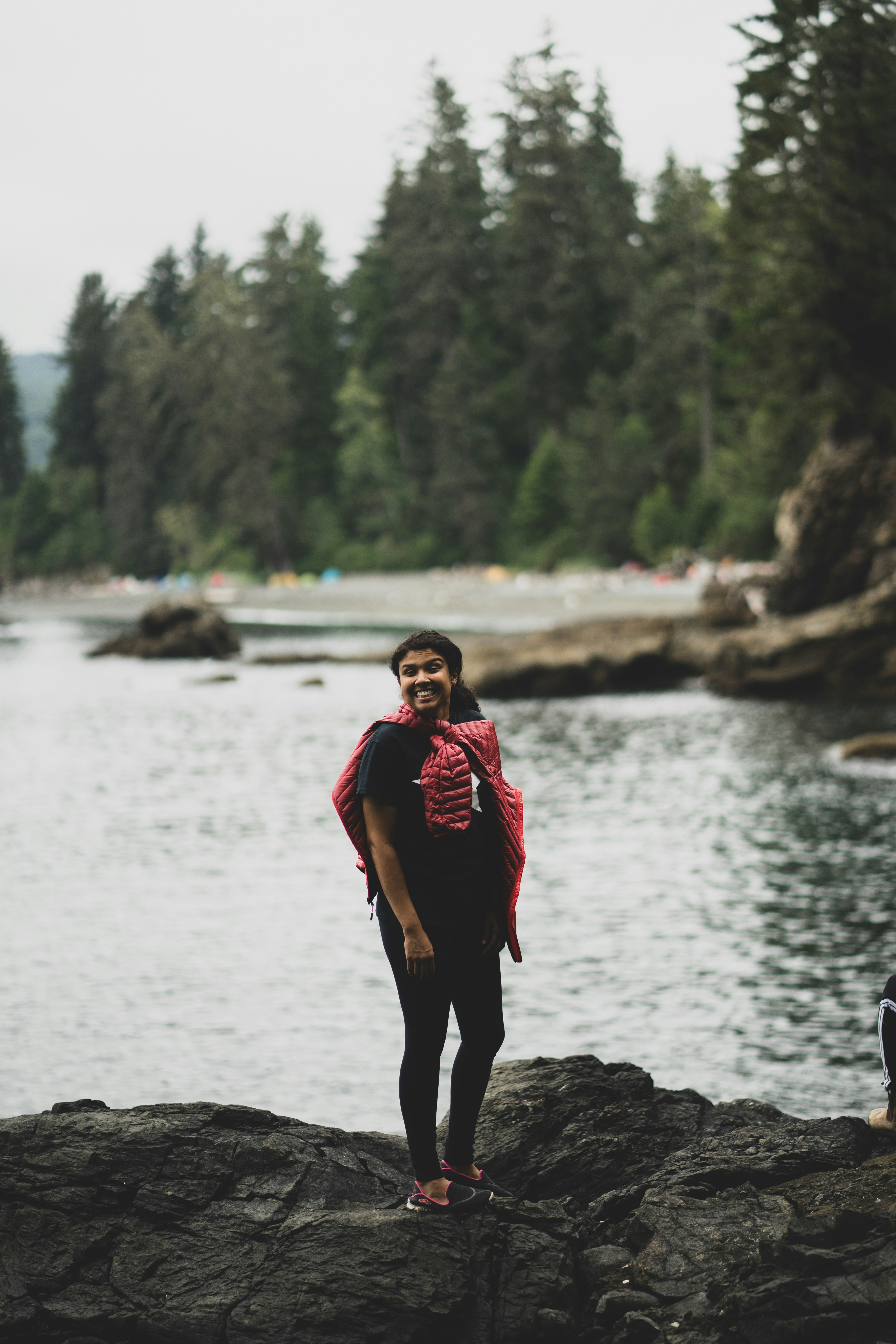 A woman in a black t-shirt and red jacket on rocky shore