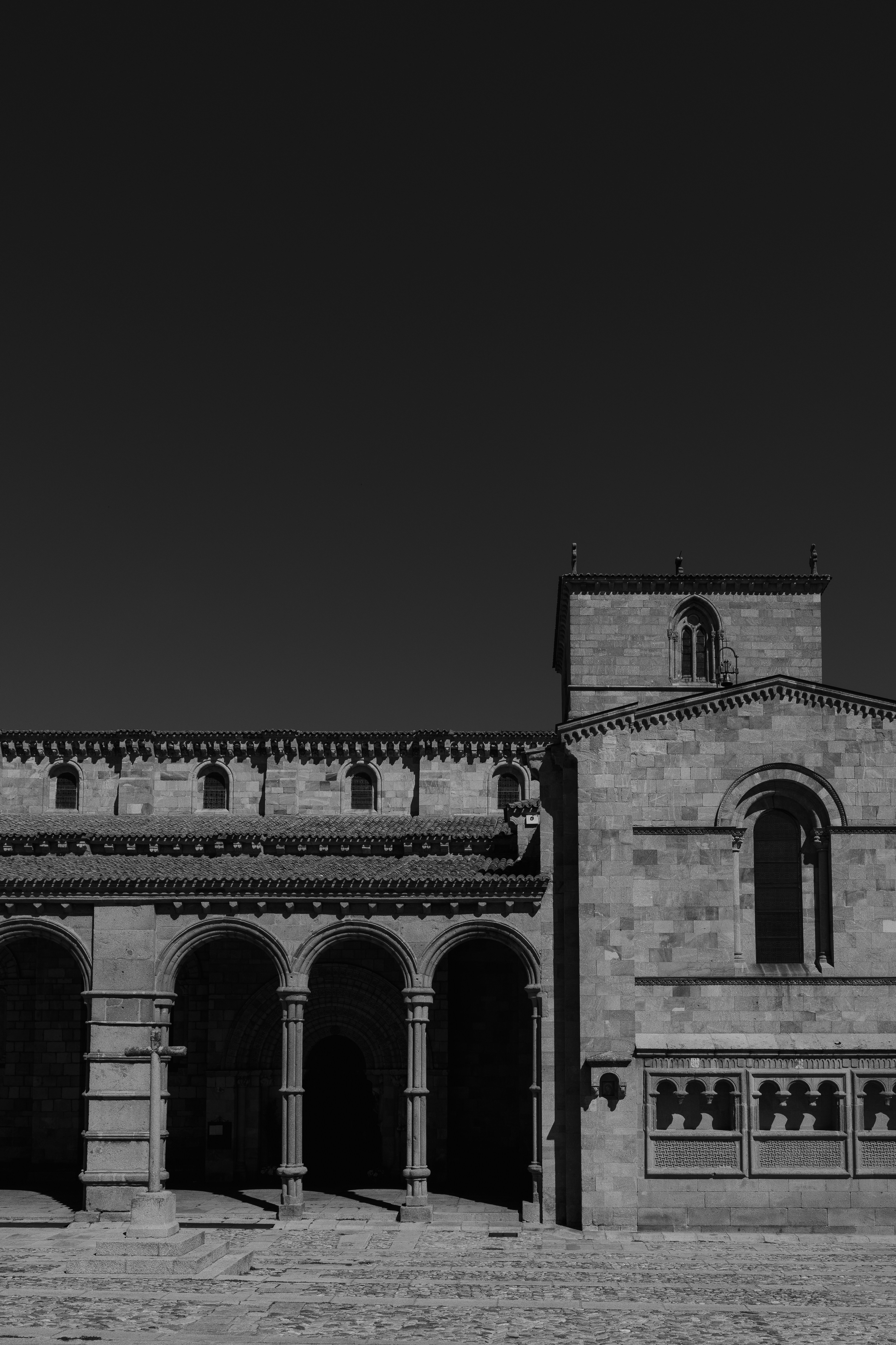 A stone Romanesque church with arched porticos and a stone cross in Avila