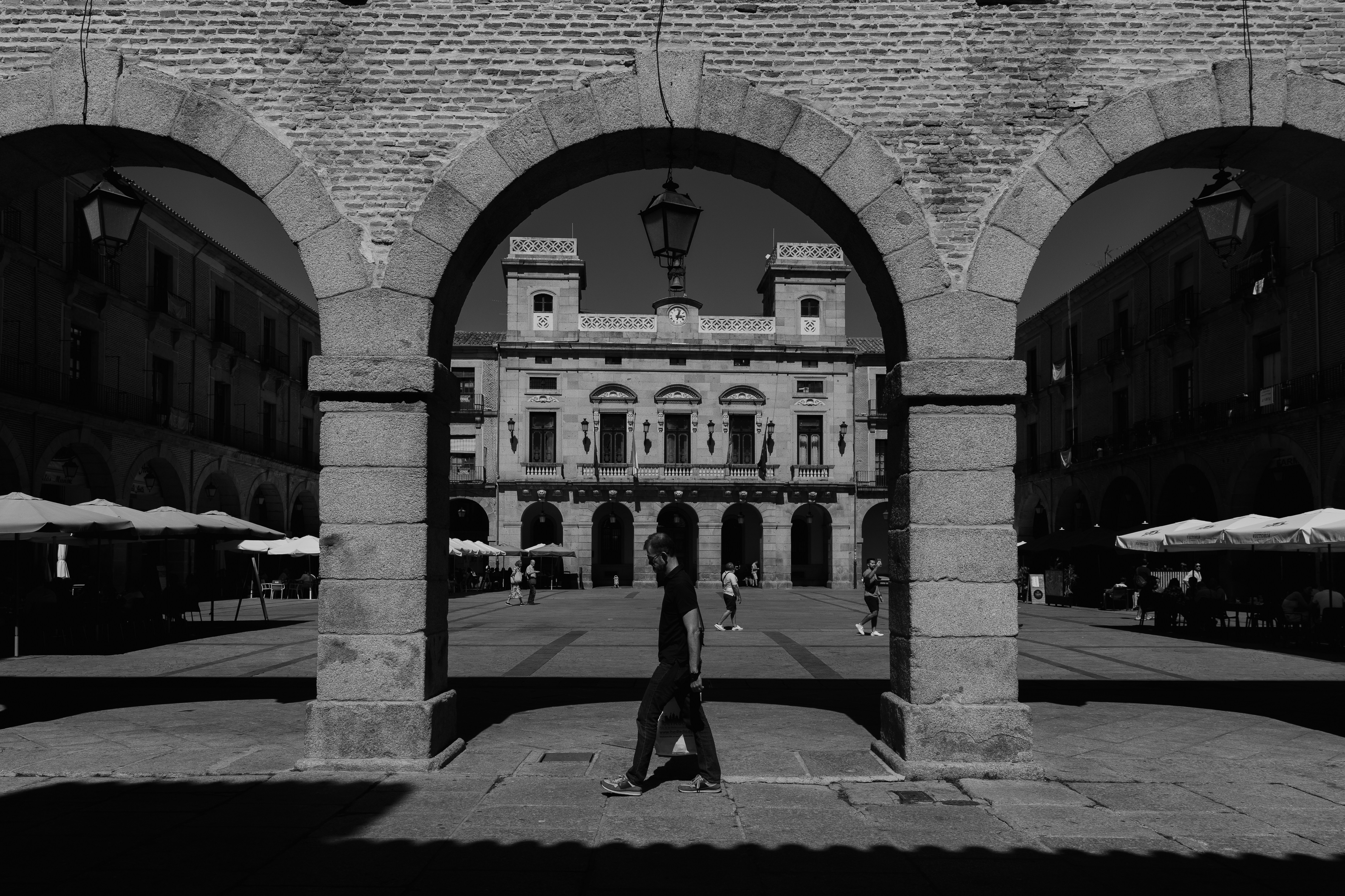 A person walking through a stone archway into a sunlit plaza in Spain