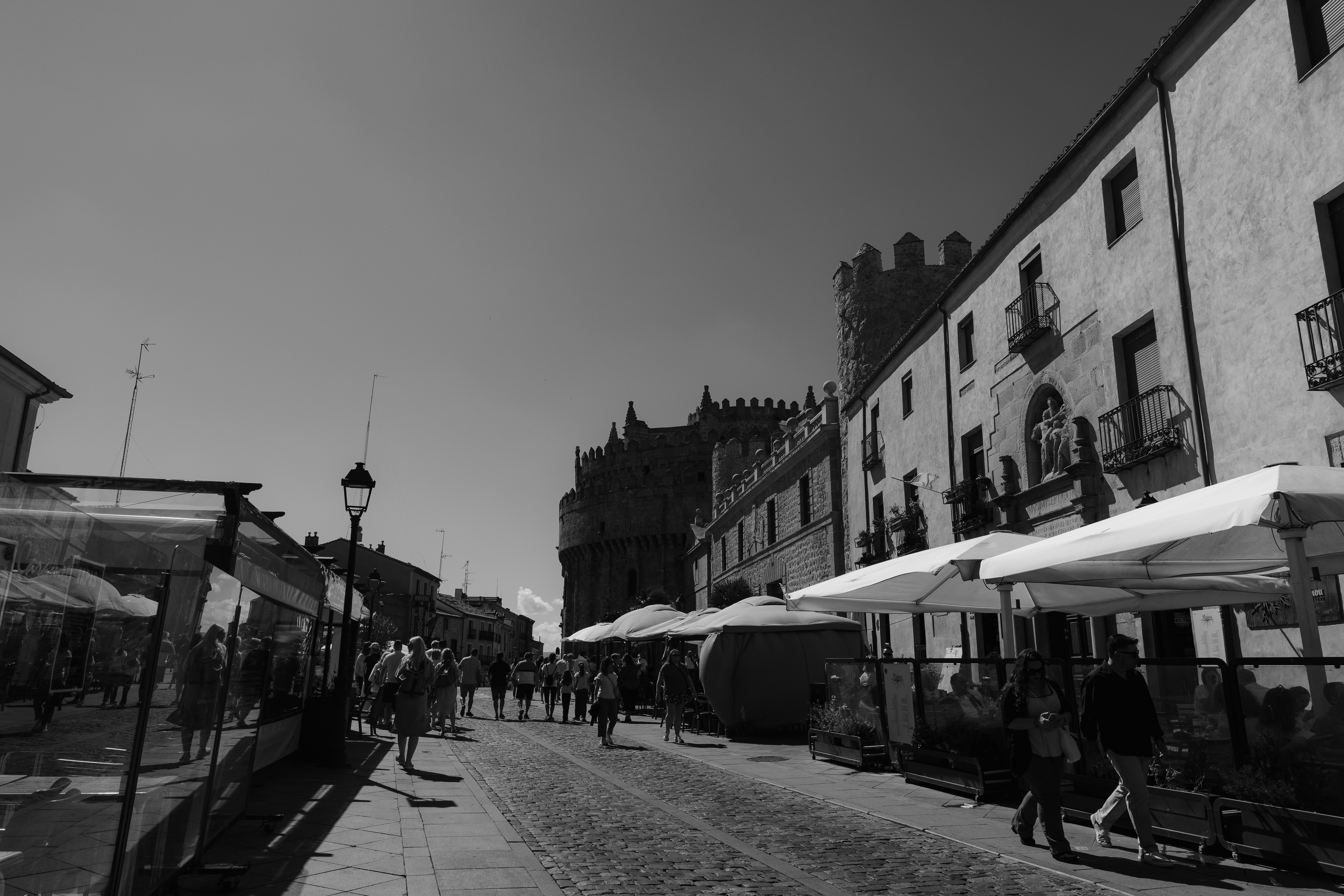 People walking on a cobblestone street lined with outdoor cafe seating and historic stone architecture